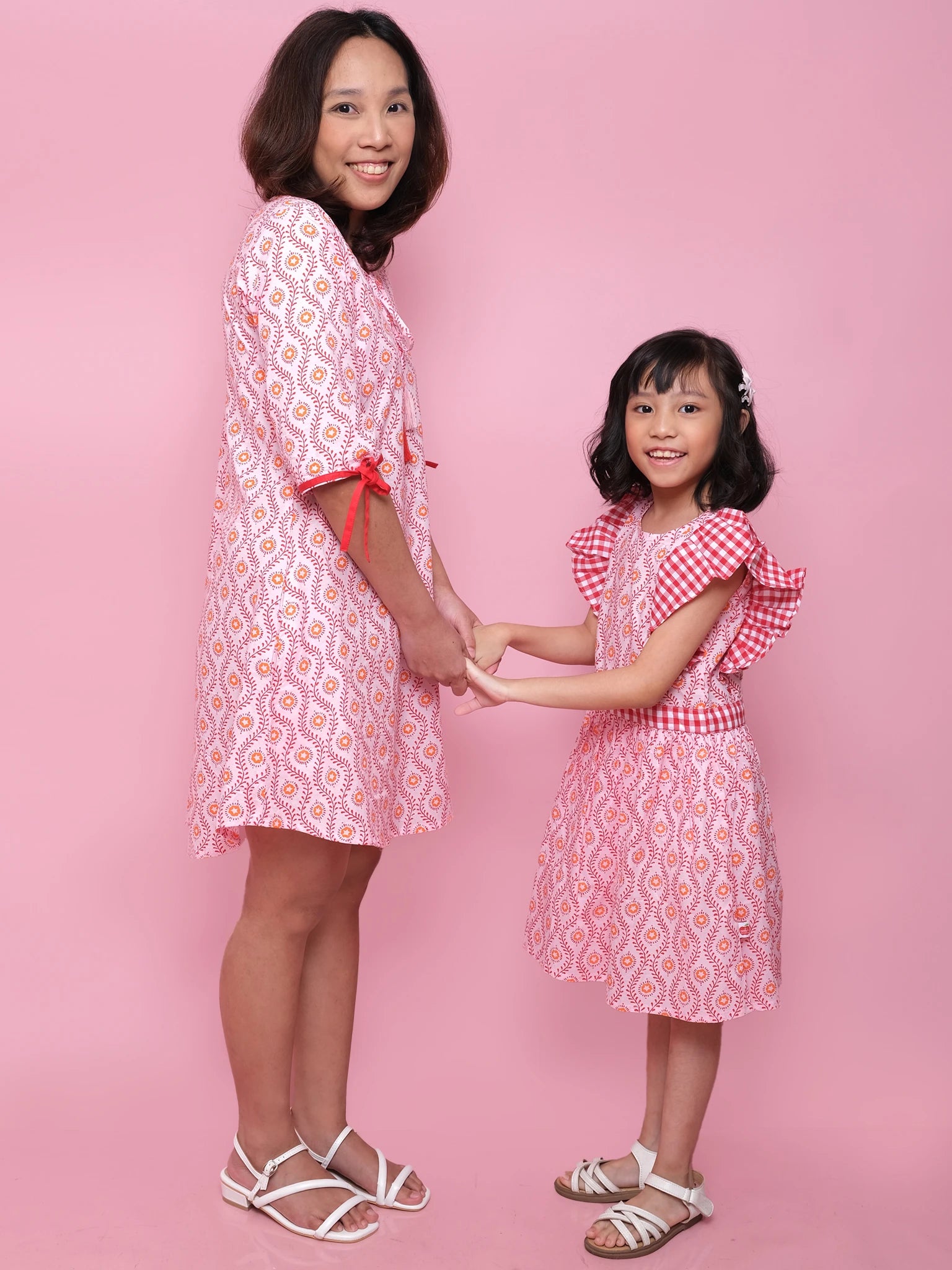 Woman and young girl holding hands wearing matching pink outfits against a pink background