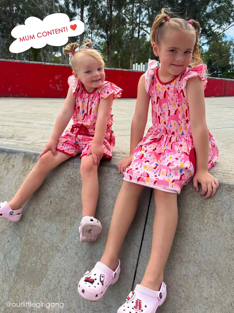 Sisters sitting together in Magical Unicorn playsuit and dress