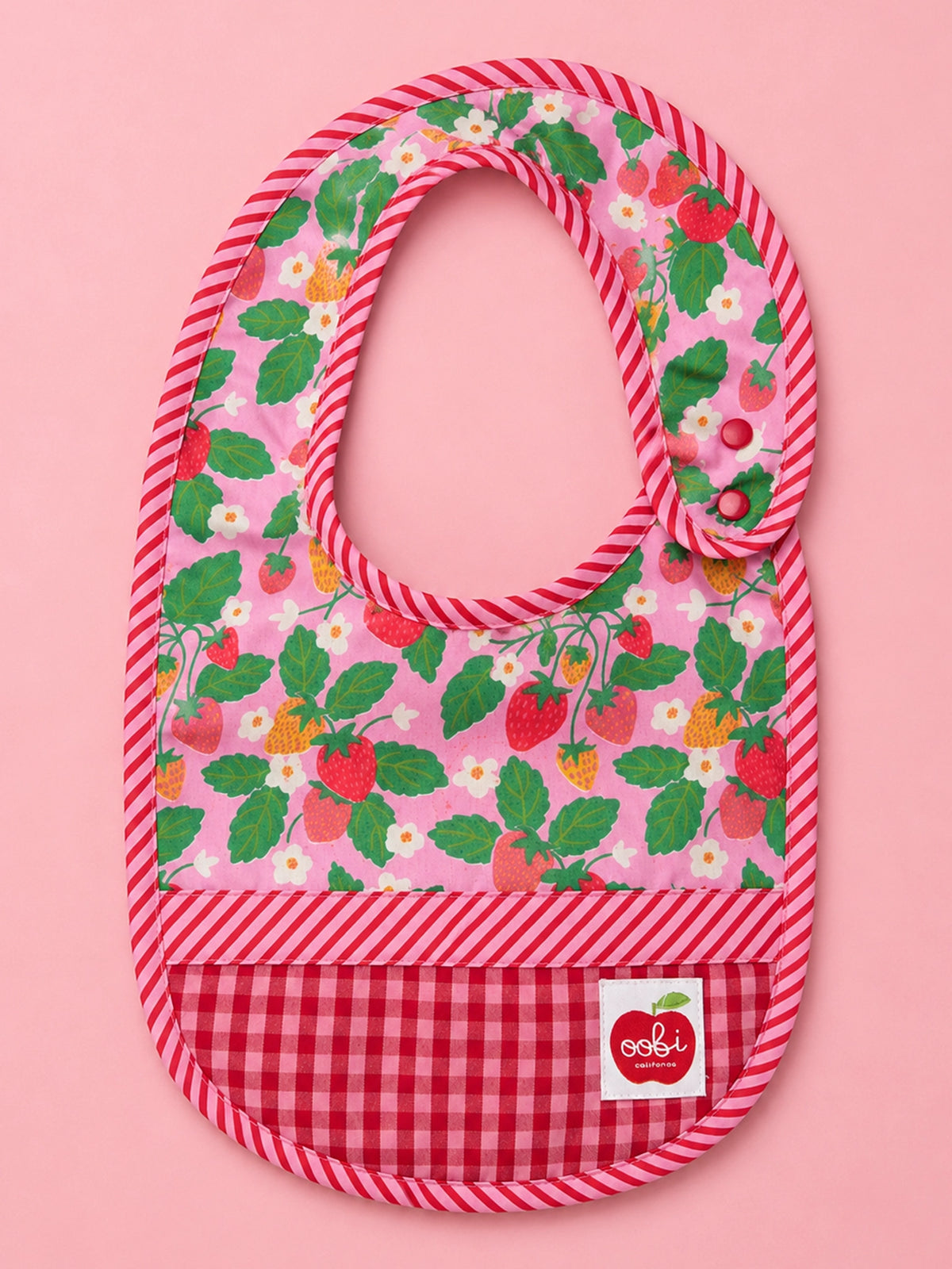 A pink baby bib with a strawberry and white flower print on the upper section, a red and white gingham pattern on the lower section, and a pink and white striped border. A small white brand label for 'oohi' is visible on the bottom right.