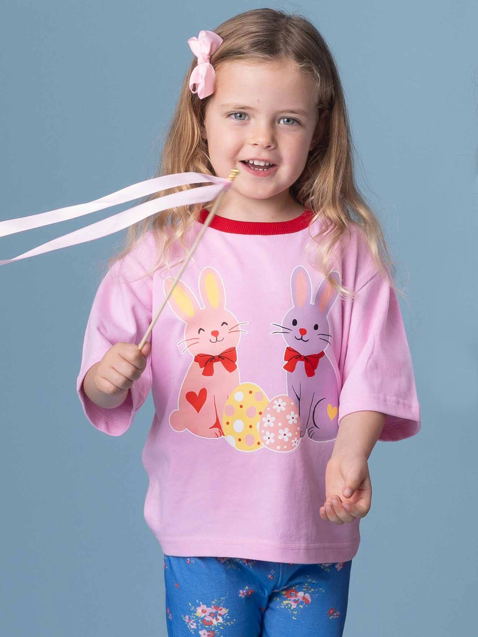 Young girl wearing a pink shirt with bunny designs against a blue background