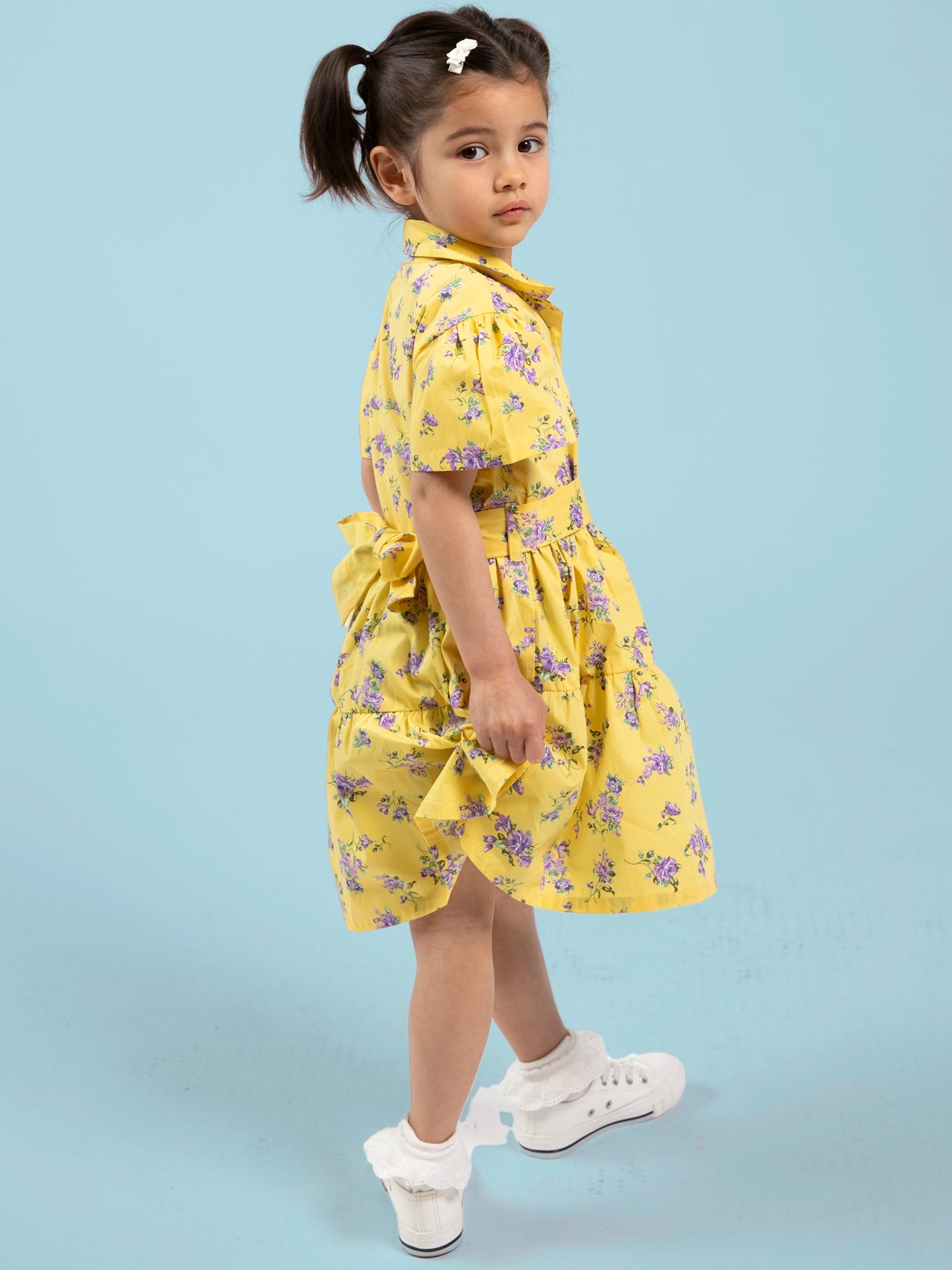 Young girl wearing a yellow floral dress against a light blue background