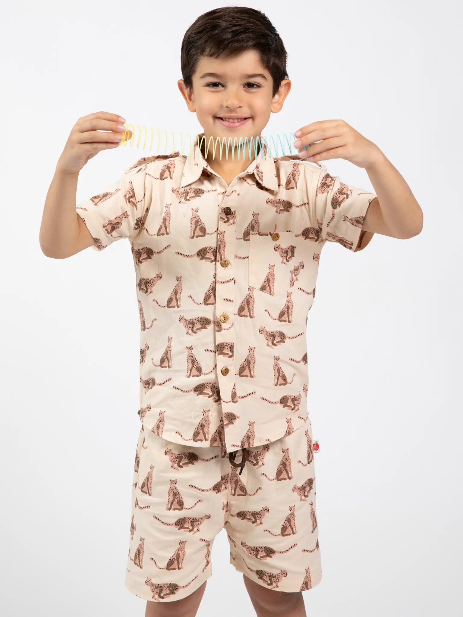 Boy wearing a beige, leopard animal-patterned collared shirt and shorts with a blue background playing with a spring toy