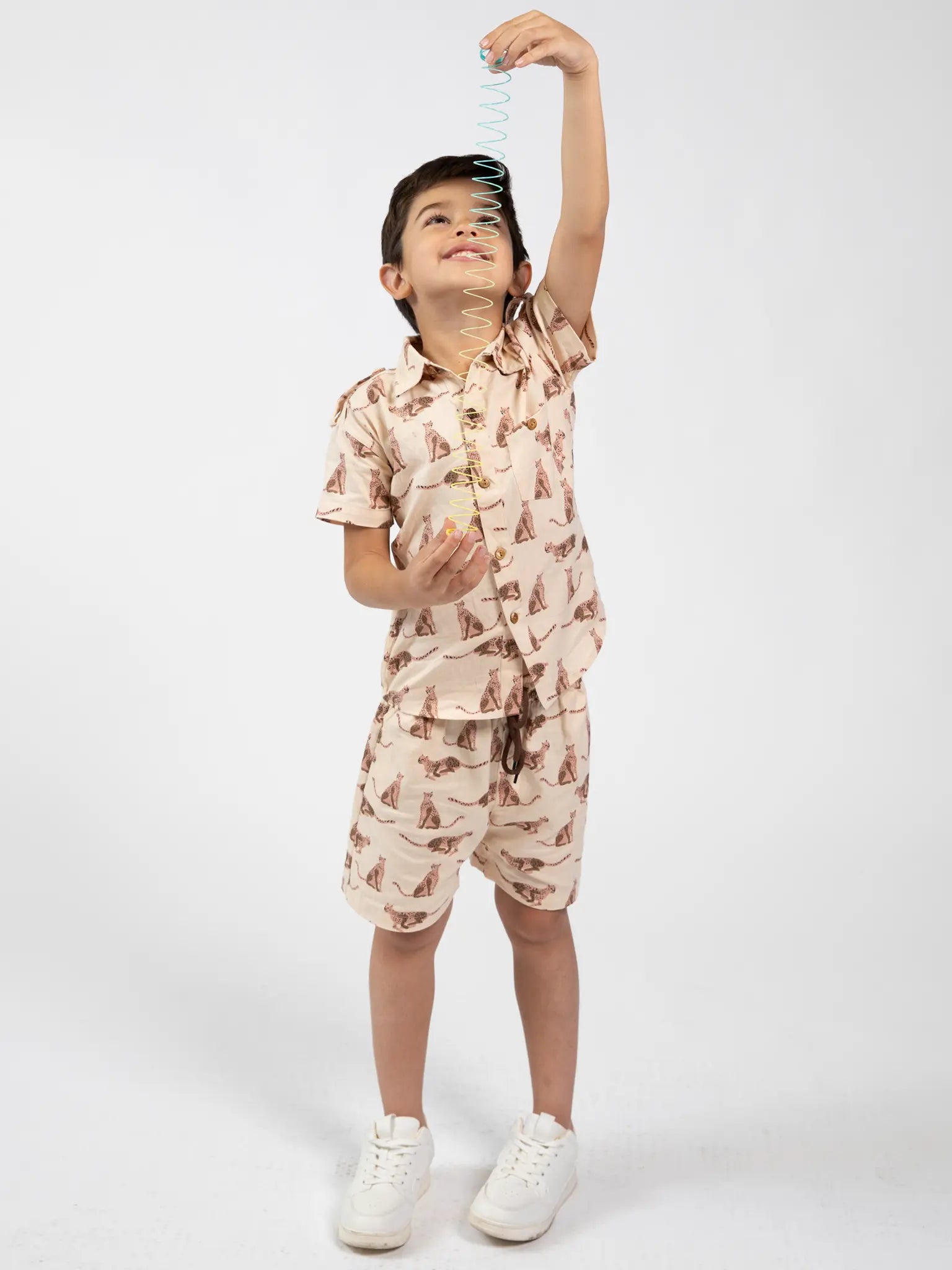 Child wearing a leopard patterned outfit playing with a spring toy on a white background