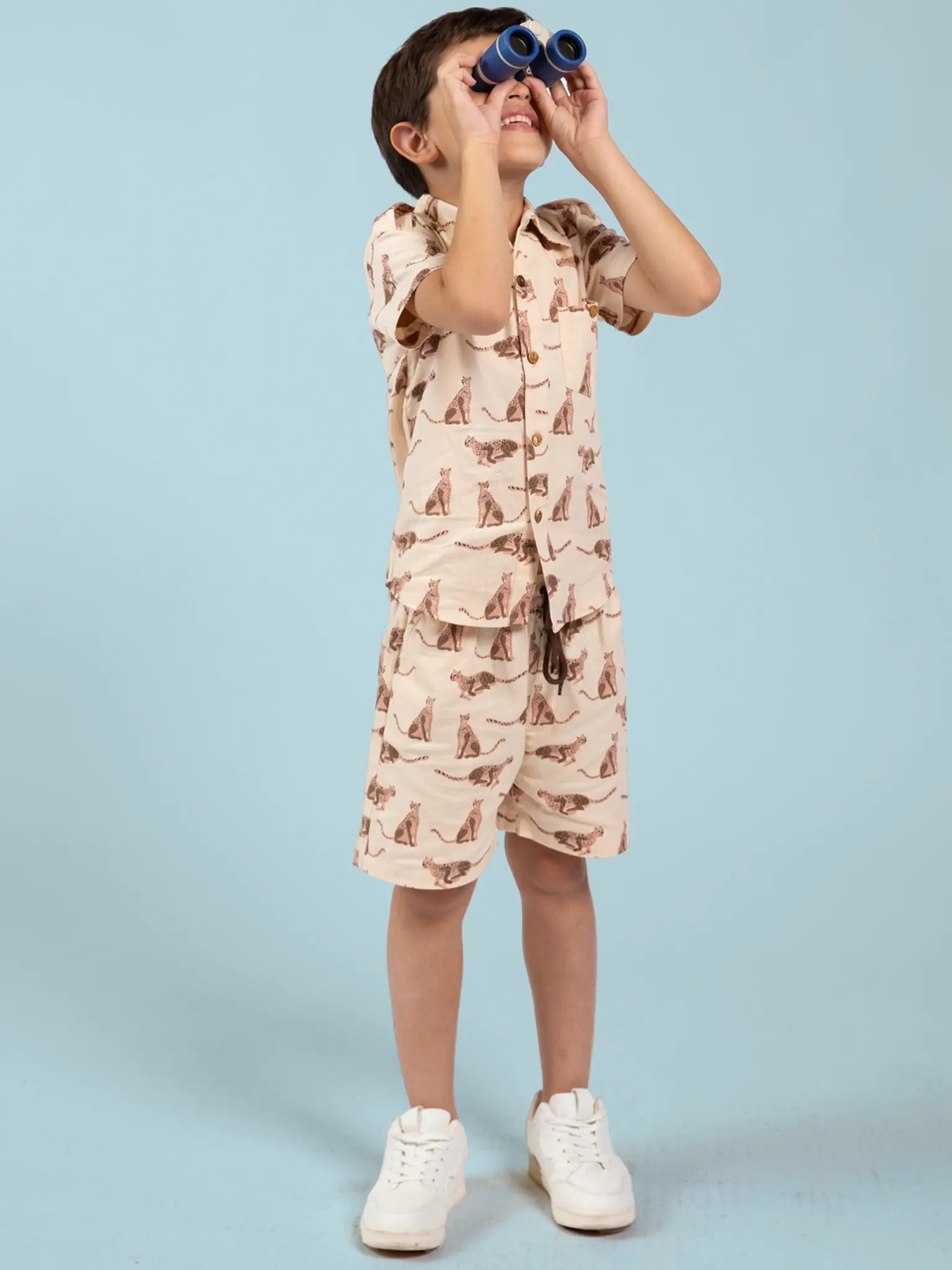 Child wearing a leopard patterned outfit with binoculars against a light blue background