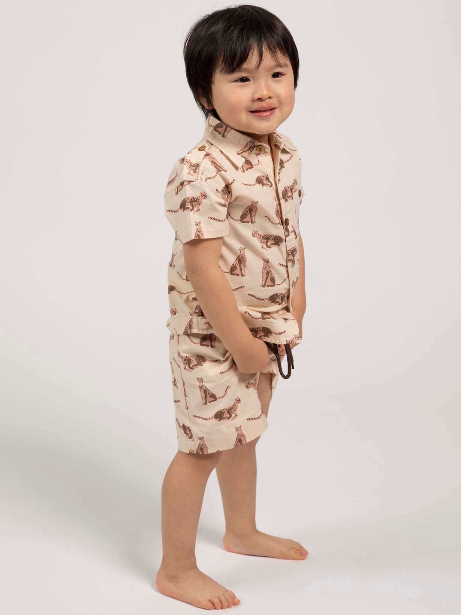 Child wearing a beige, leopard animal-patterned collared shirt and shorts