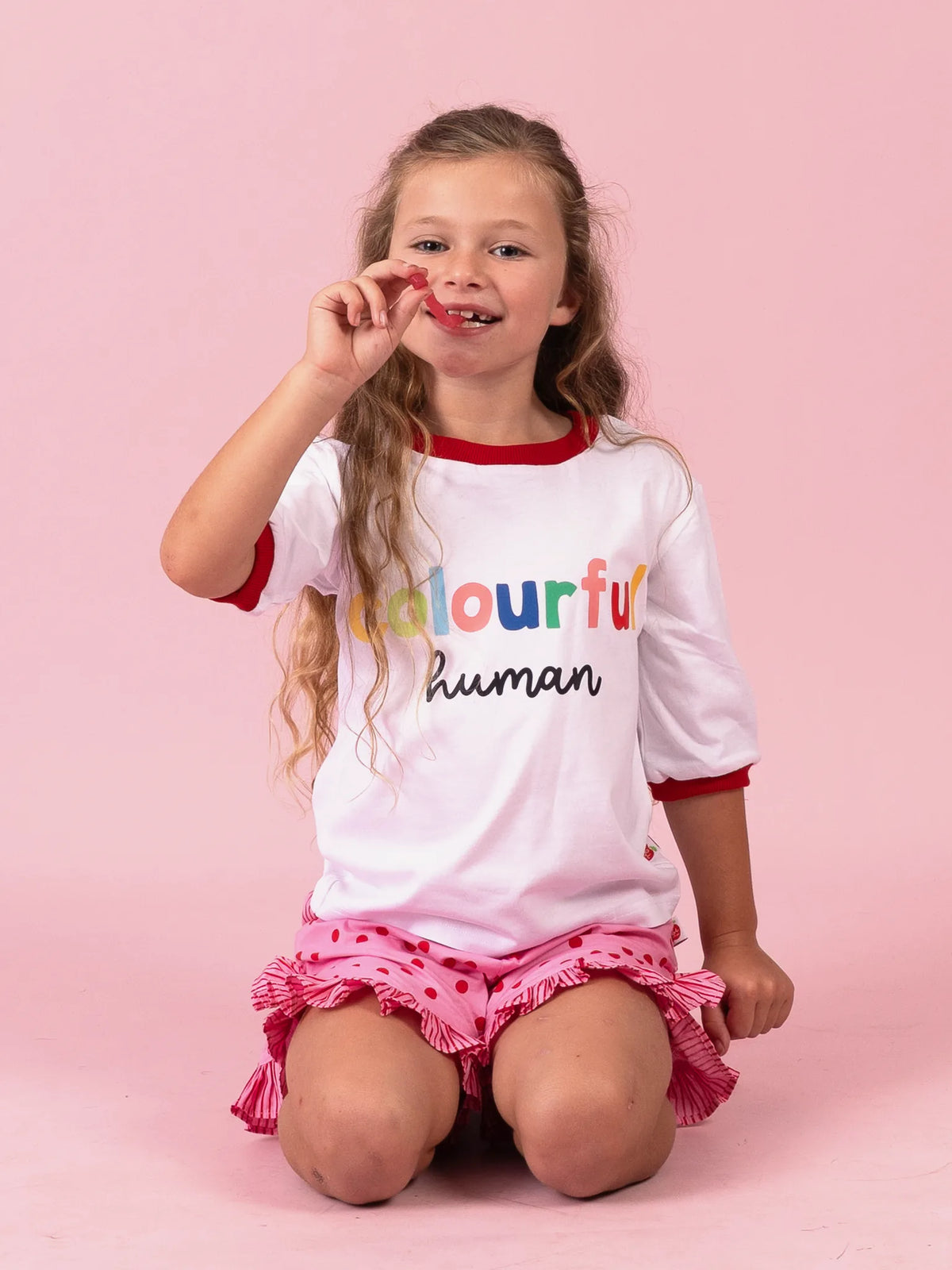 Girl kneeling in the white Colourful Human tee and Pink & Red Dots ruffle shorts