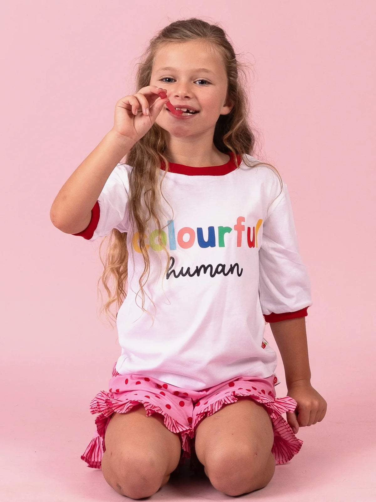 Girl kneeling in the white Colourful Human tee and Pink & Red Dots ruffle shorts