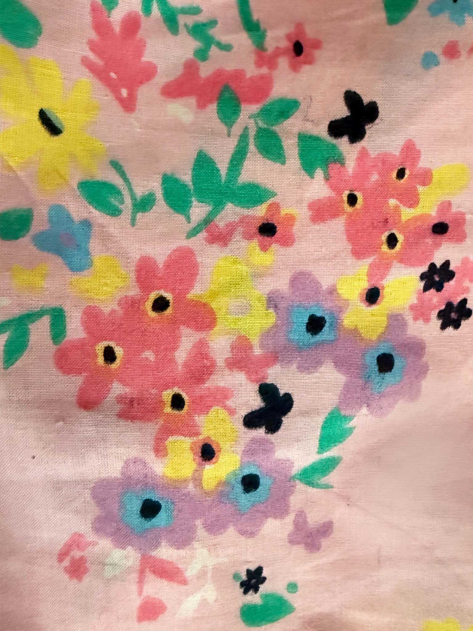 A close-up of the Confetti Floral Lacy Dress by Confetti Floral, showing cotton fabric with a floral pattern in pink, yellow, purple, green, and black on a light pink background.