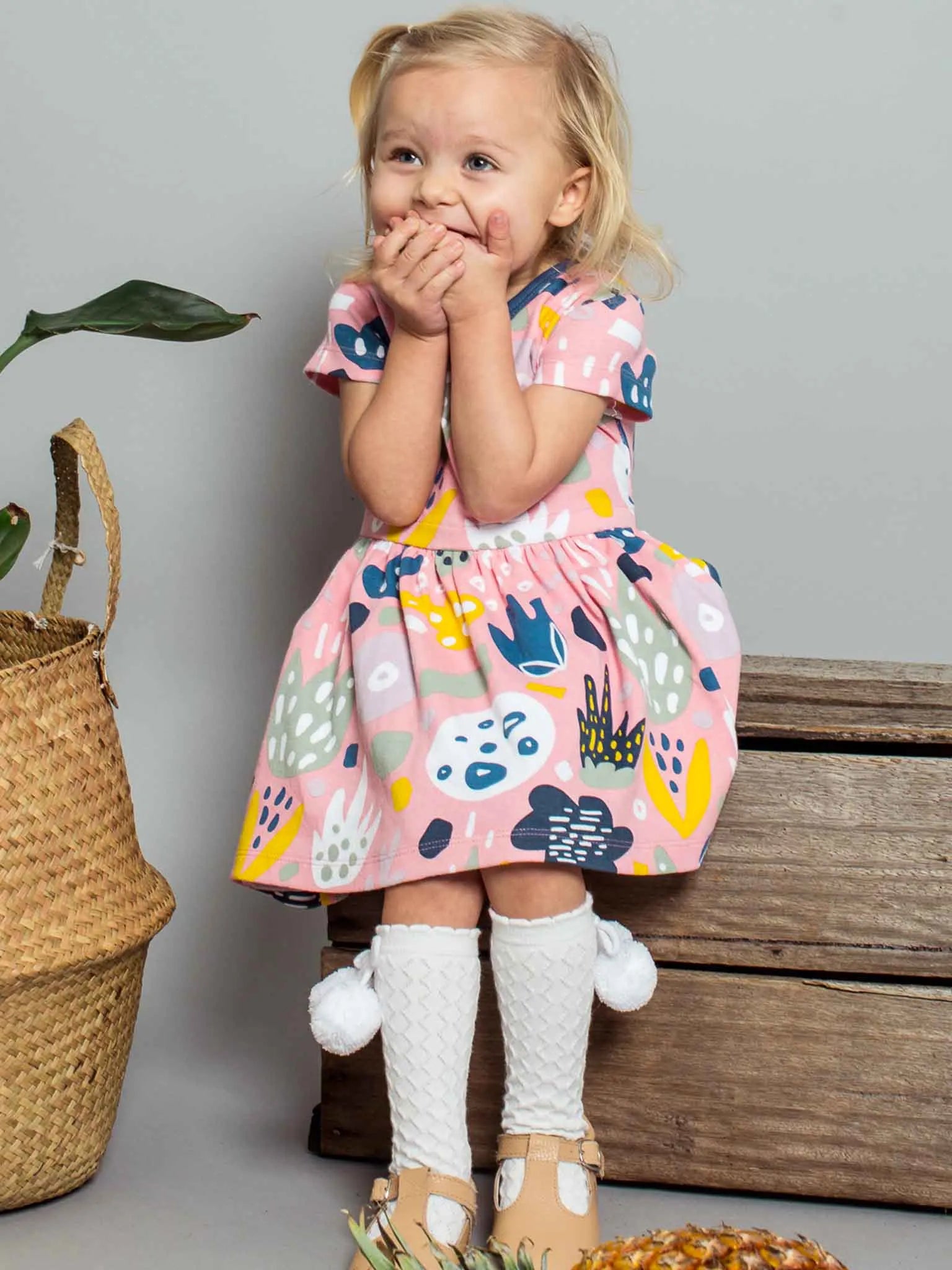 Smiling girl wearing a pink jungle print dress and white pom pom socks
