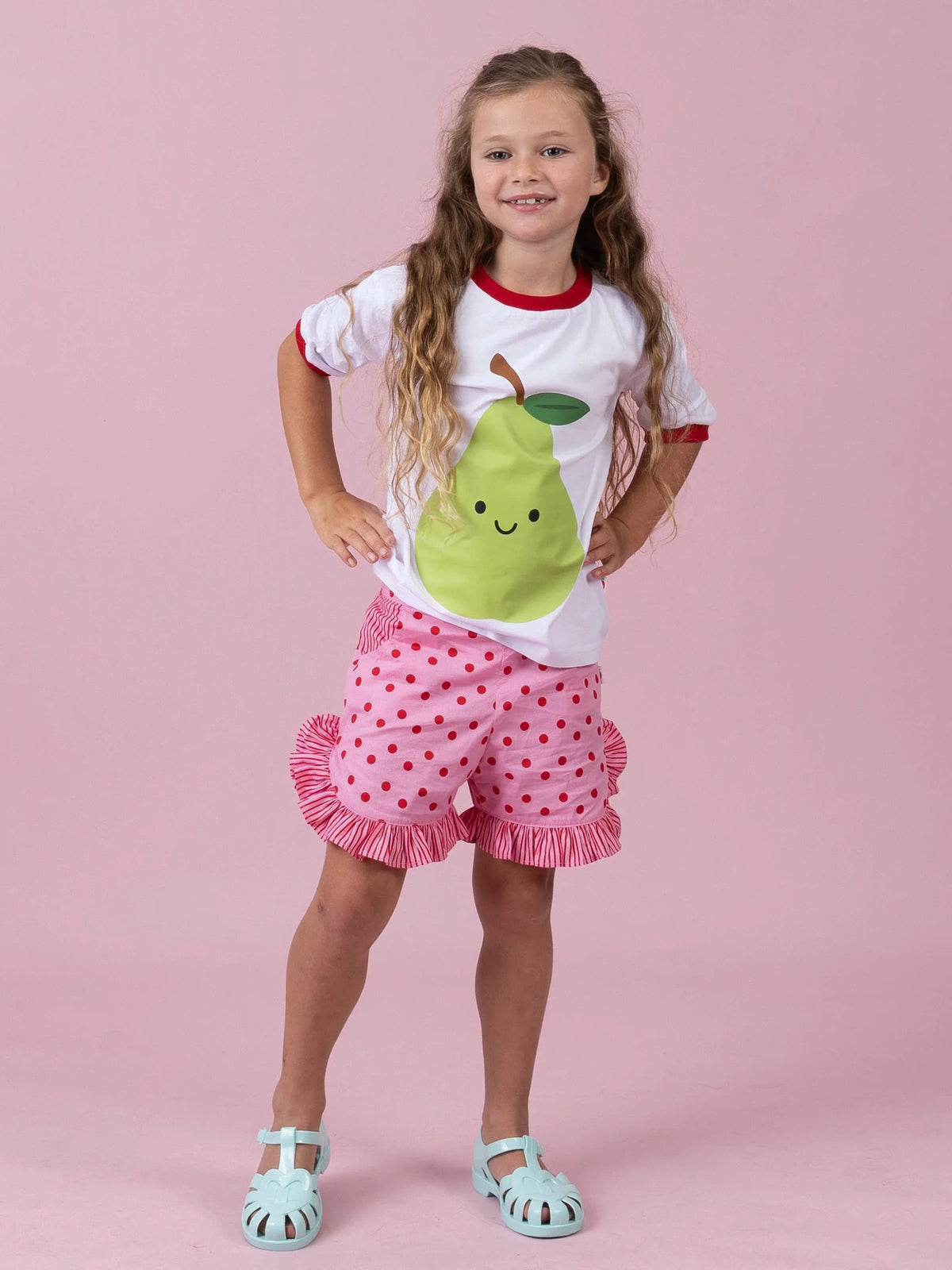 Girl in the white Happy Pear tee and Pink & Red Dots ruffle shorts, hands on hips