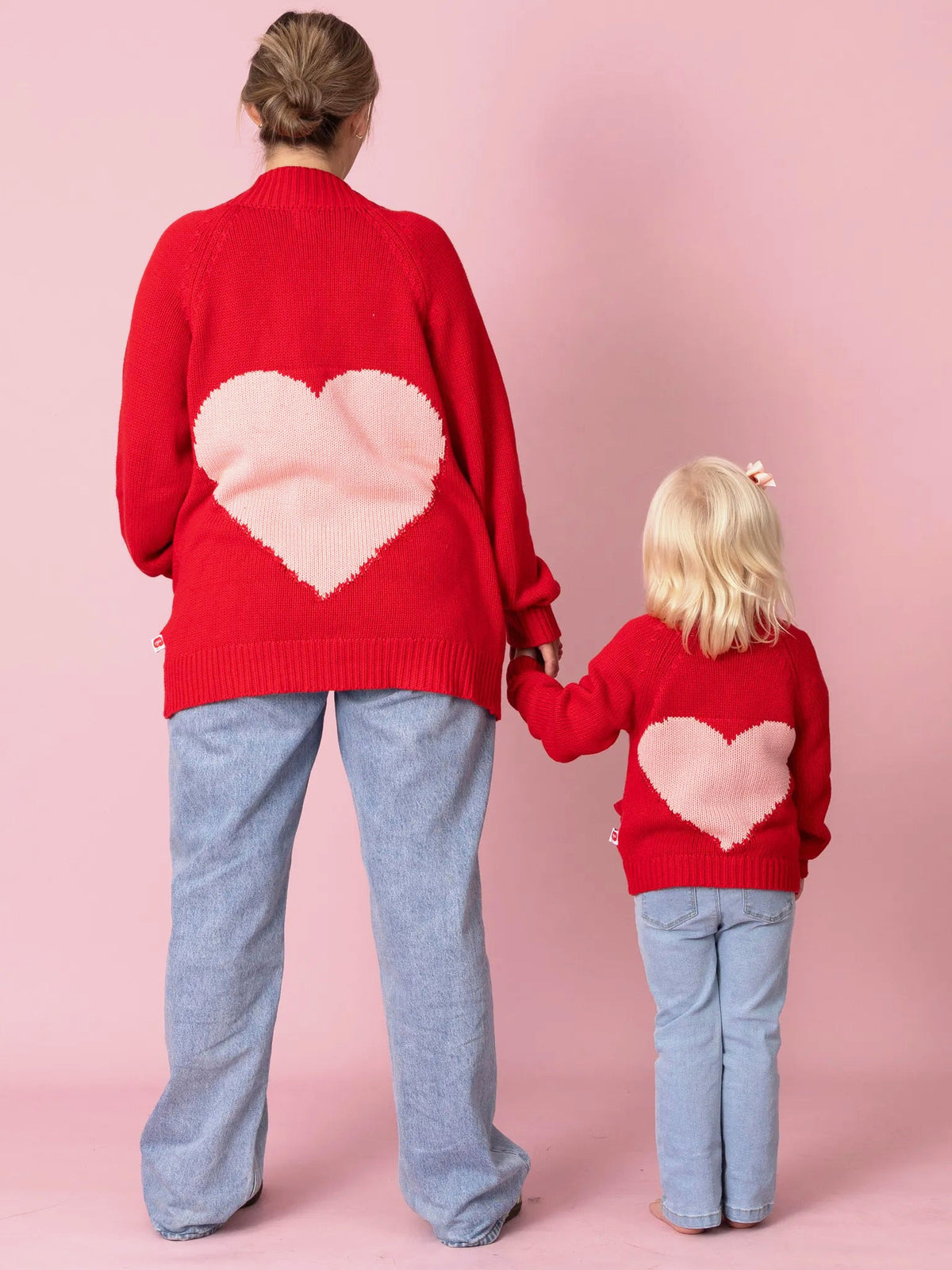 Two people wearing red sweaters with pink heart designs on a pink background
