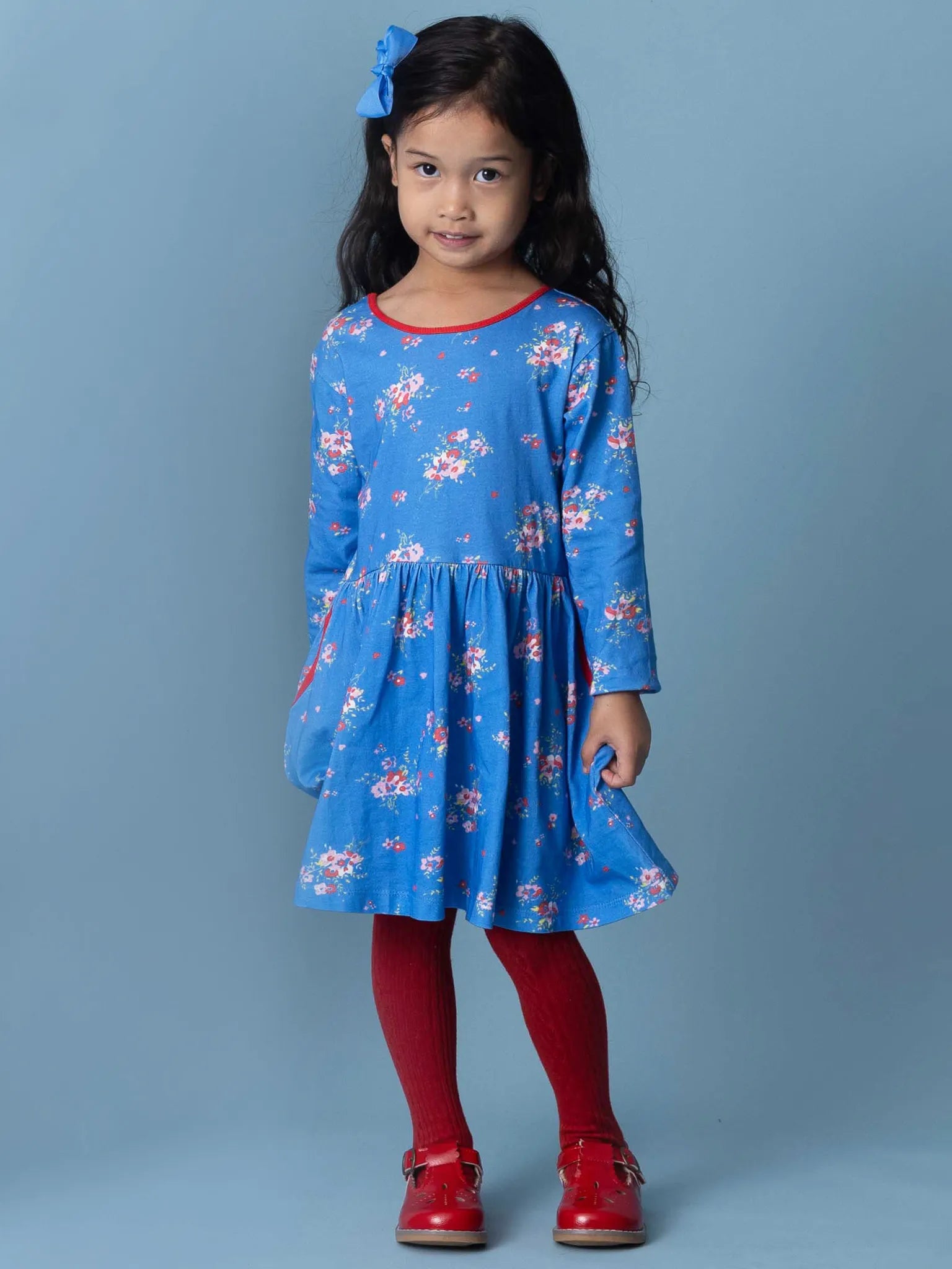 Young girl wearing a blue floral dress with red accents against a gray background