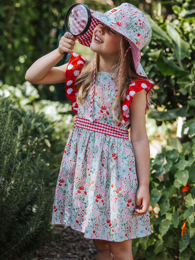 Young girl in a Bunny dress and polka dot hat exploring nature with a magnifying glass.