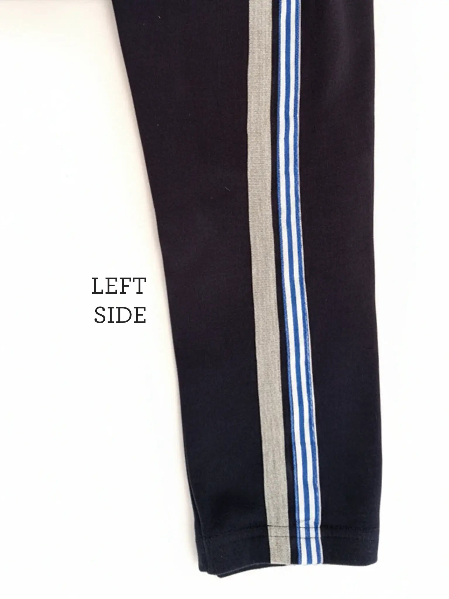 A close-up of the left side of Essentials Navy Jersey 2 Stripe Pants shows a wide gray stripe with two thin blue and white stripes; "LEFT SIDE" is printed beside the leg.