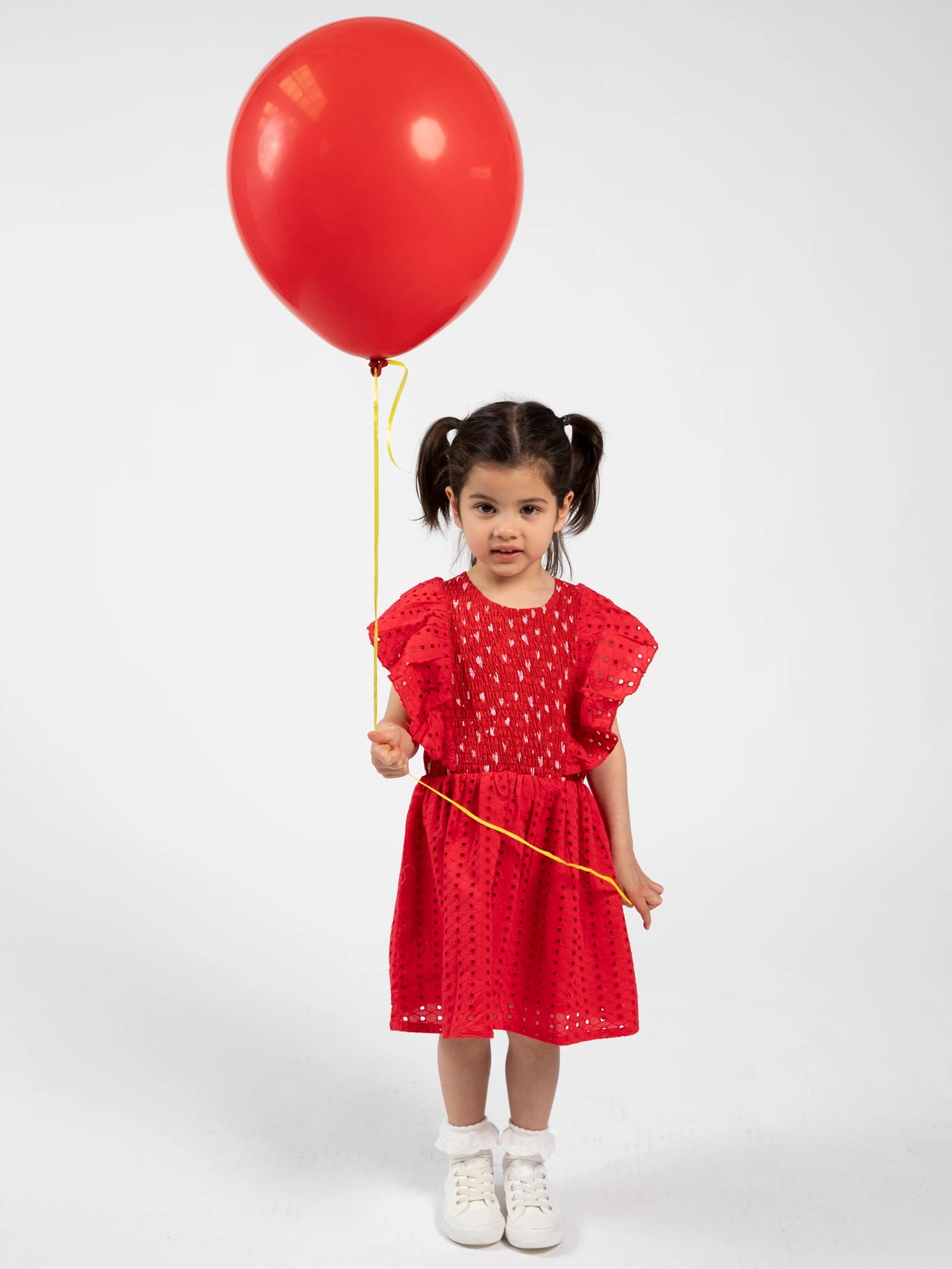 Child in a red dress holding a red balloon against a white background