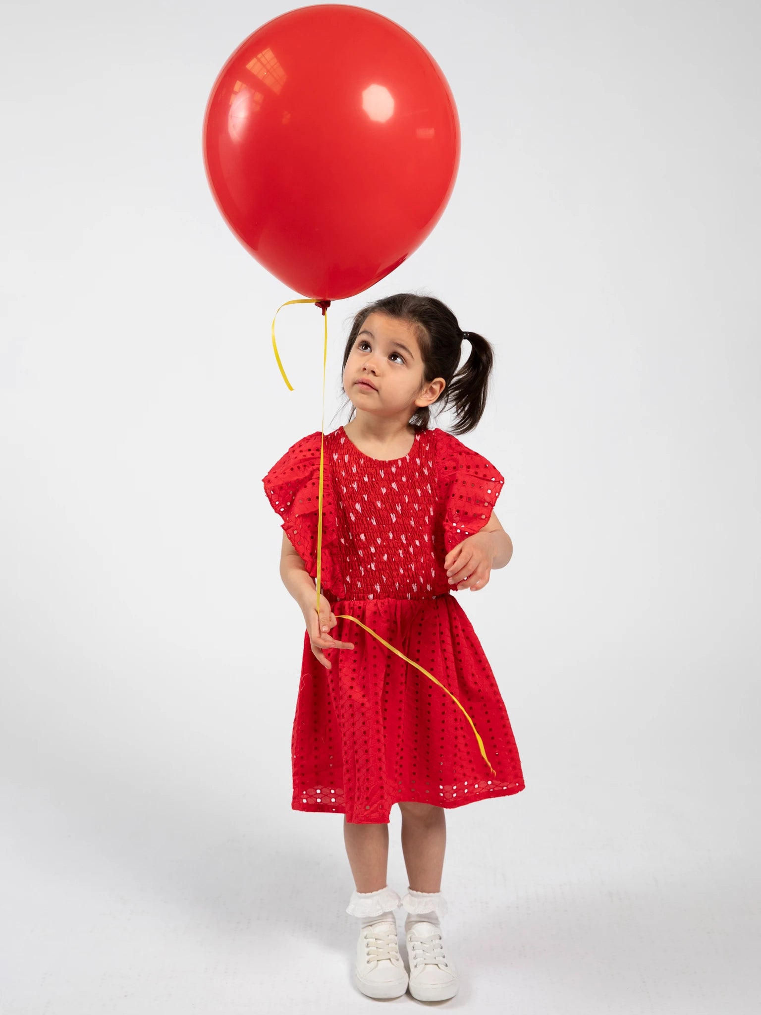 Child in a red dress holding a red balloon against a white background