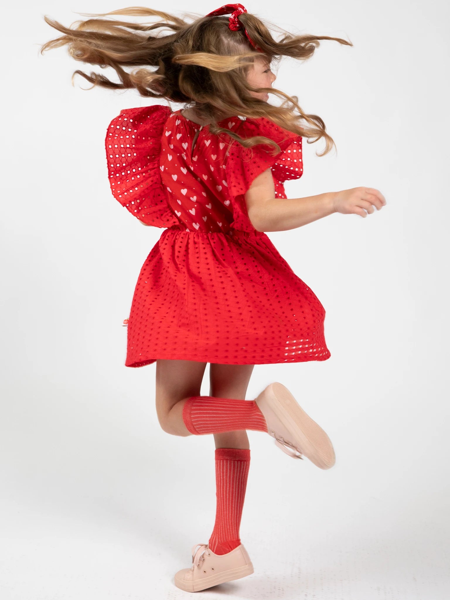 A young girl twirls in the Hearts Red Lace Party Dress with Ruched Bodice, featuring heart patterns—perfect for special occasions.