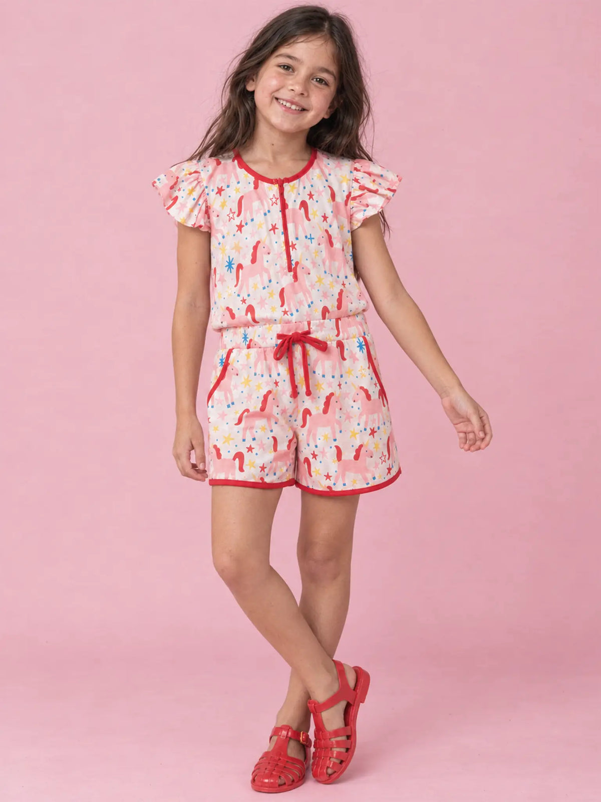 Girl in Magical Unicorn playsuit with red sandals, front view
