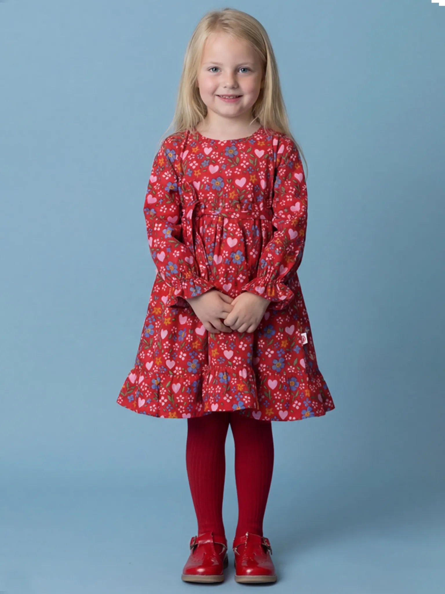 Young girl wearing a red floral dress against a blue background