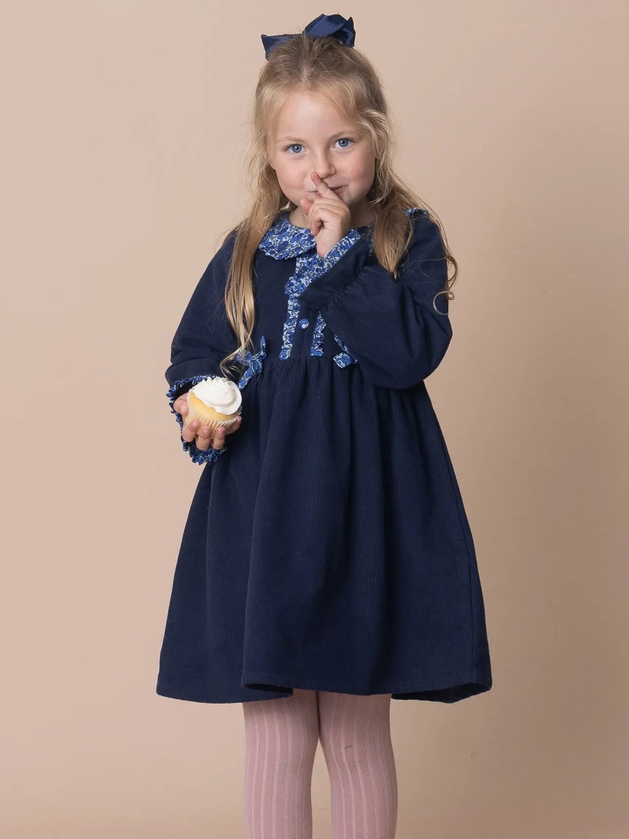 Young girl in a navy dress with floral embroidery on a beige background