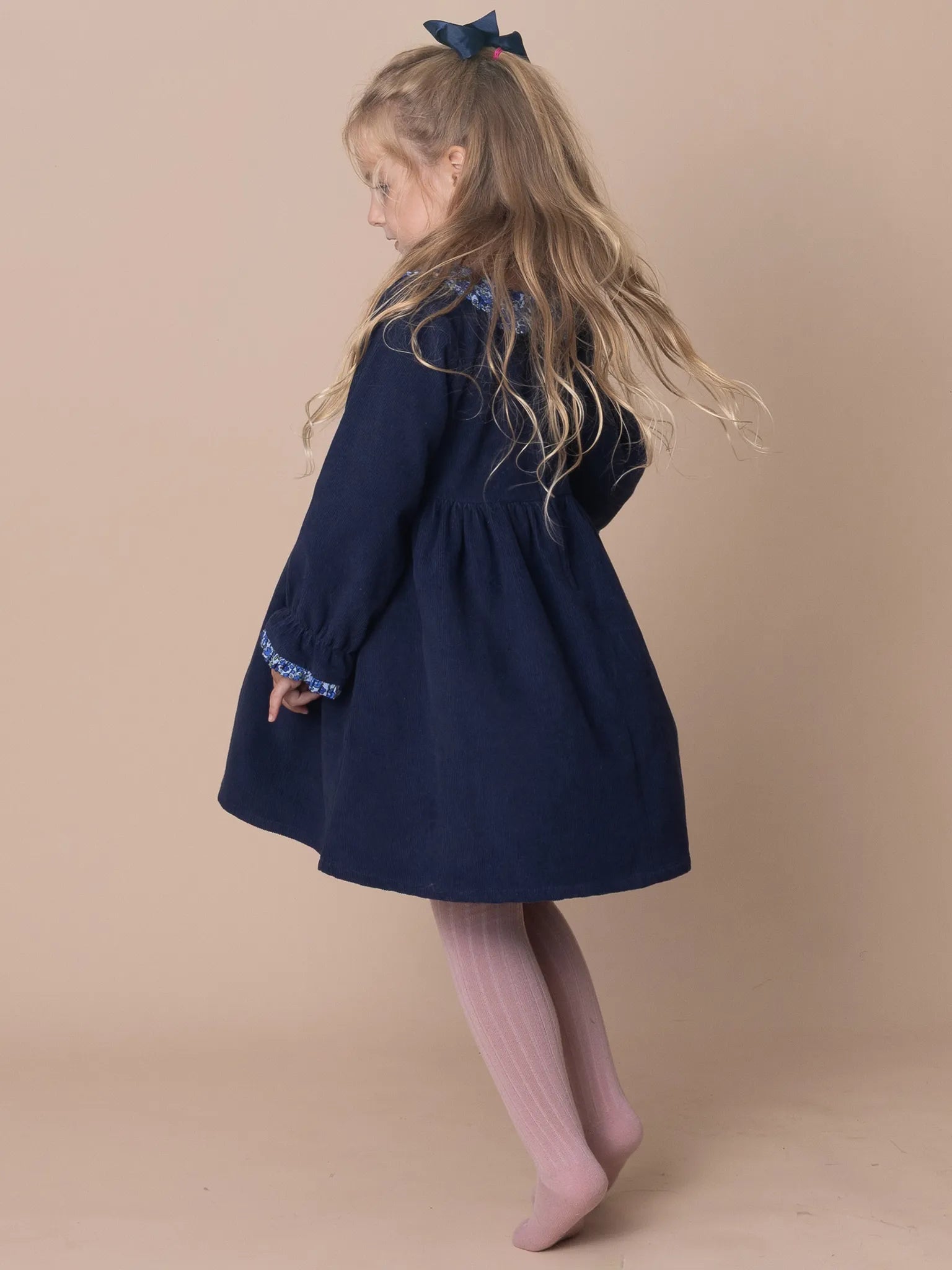 Young girl wearing a navy dress with pink tights on a beige background