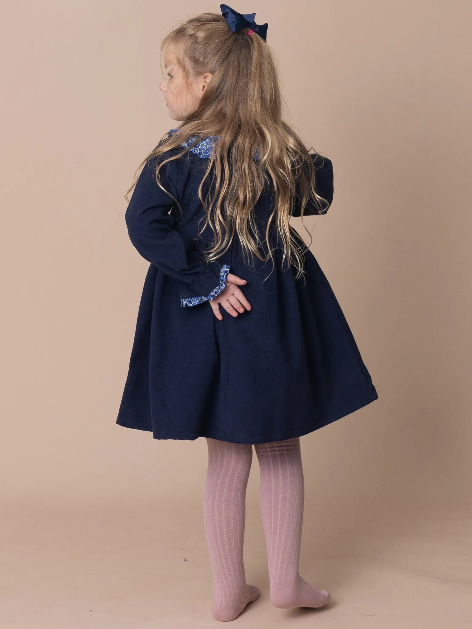 Child wearing a navy blue dress with floral details on a beige background
