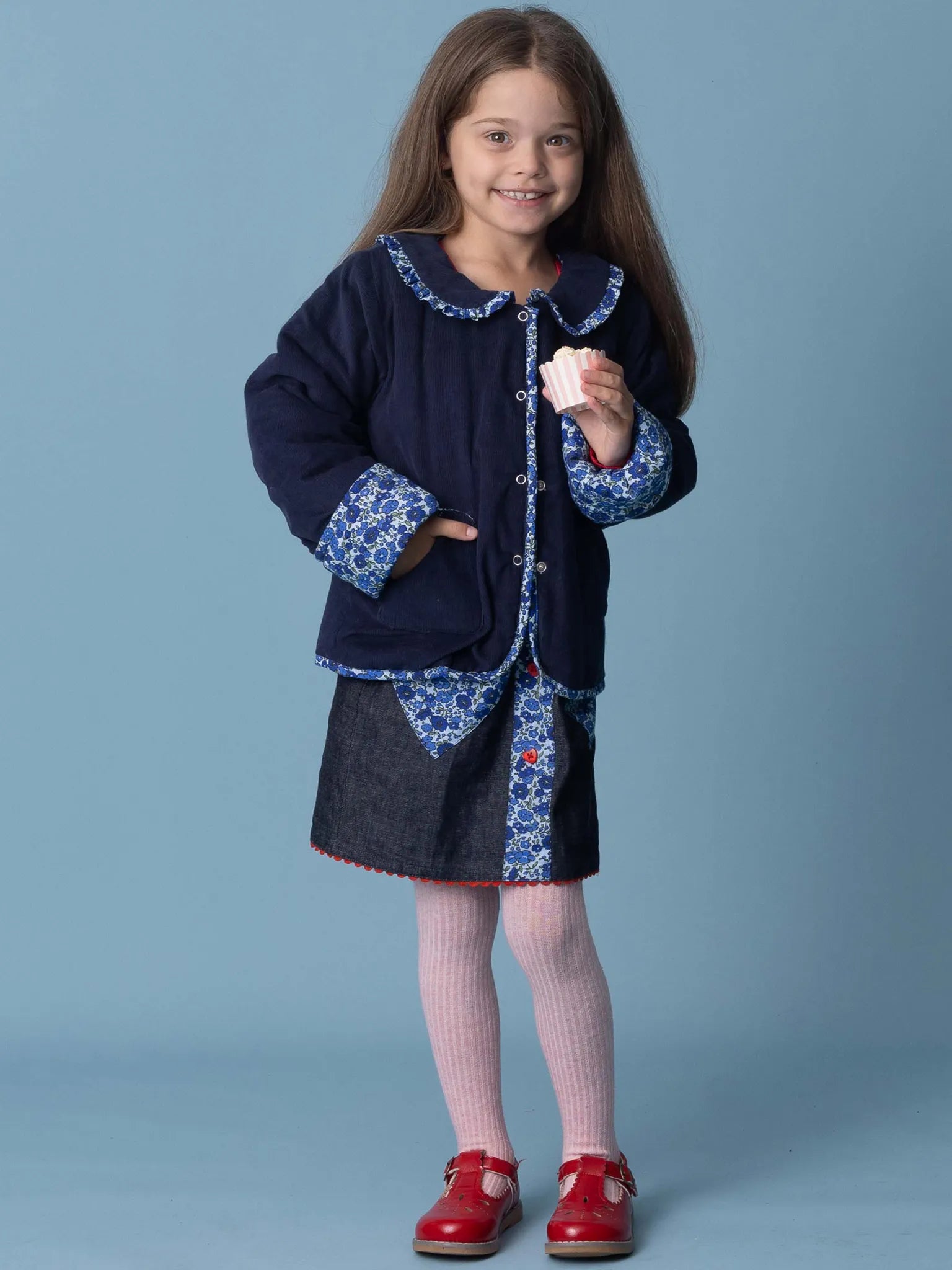 Young girl wearing a navy coat with floral patterns on a blue background