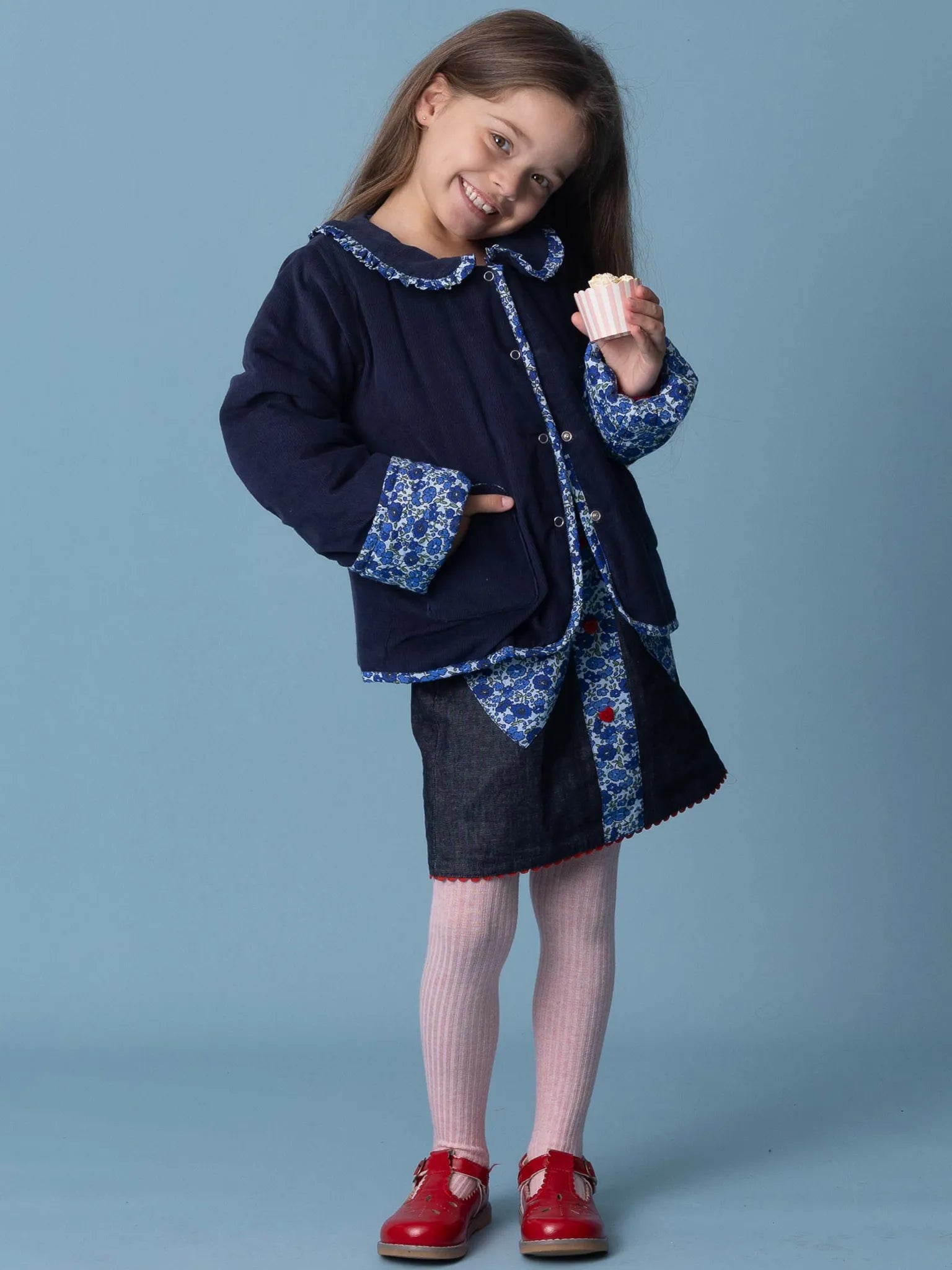 Young girl wearing a navy coat with floral patterns on a blue background