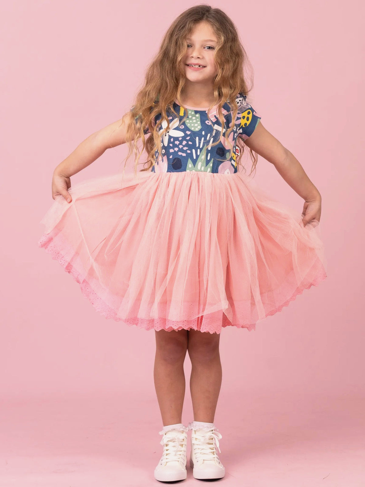 Girl holding out the tulle skirt of her Navy Jungle tutu dress