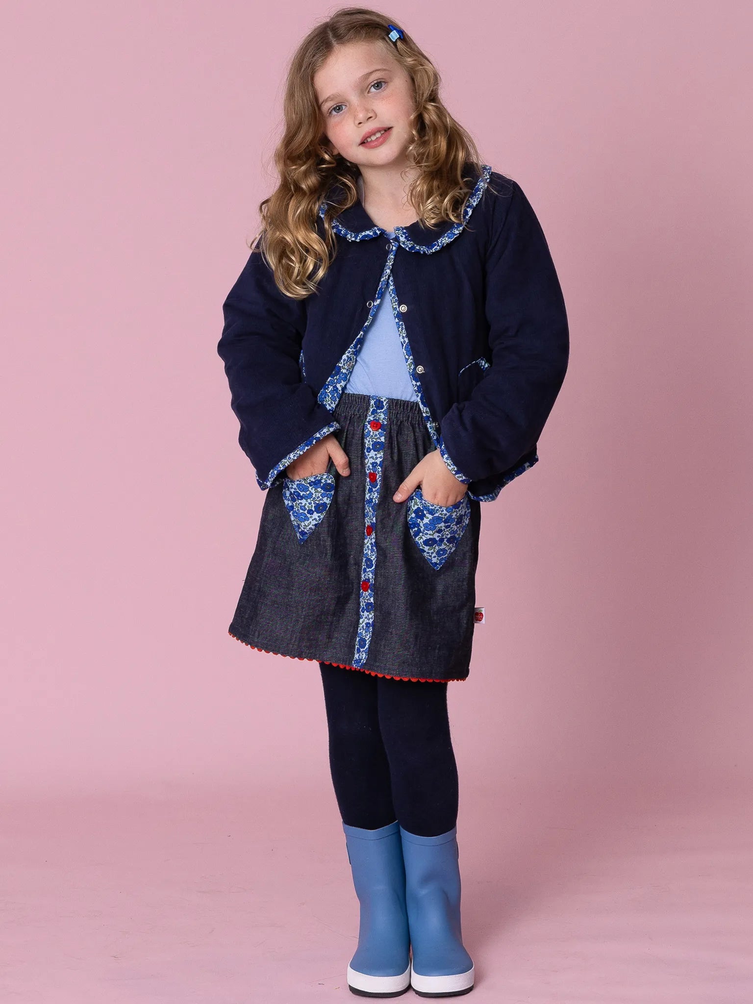 Young girl wearing a blue coat with denim patches on a pink background
