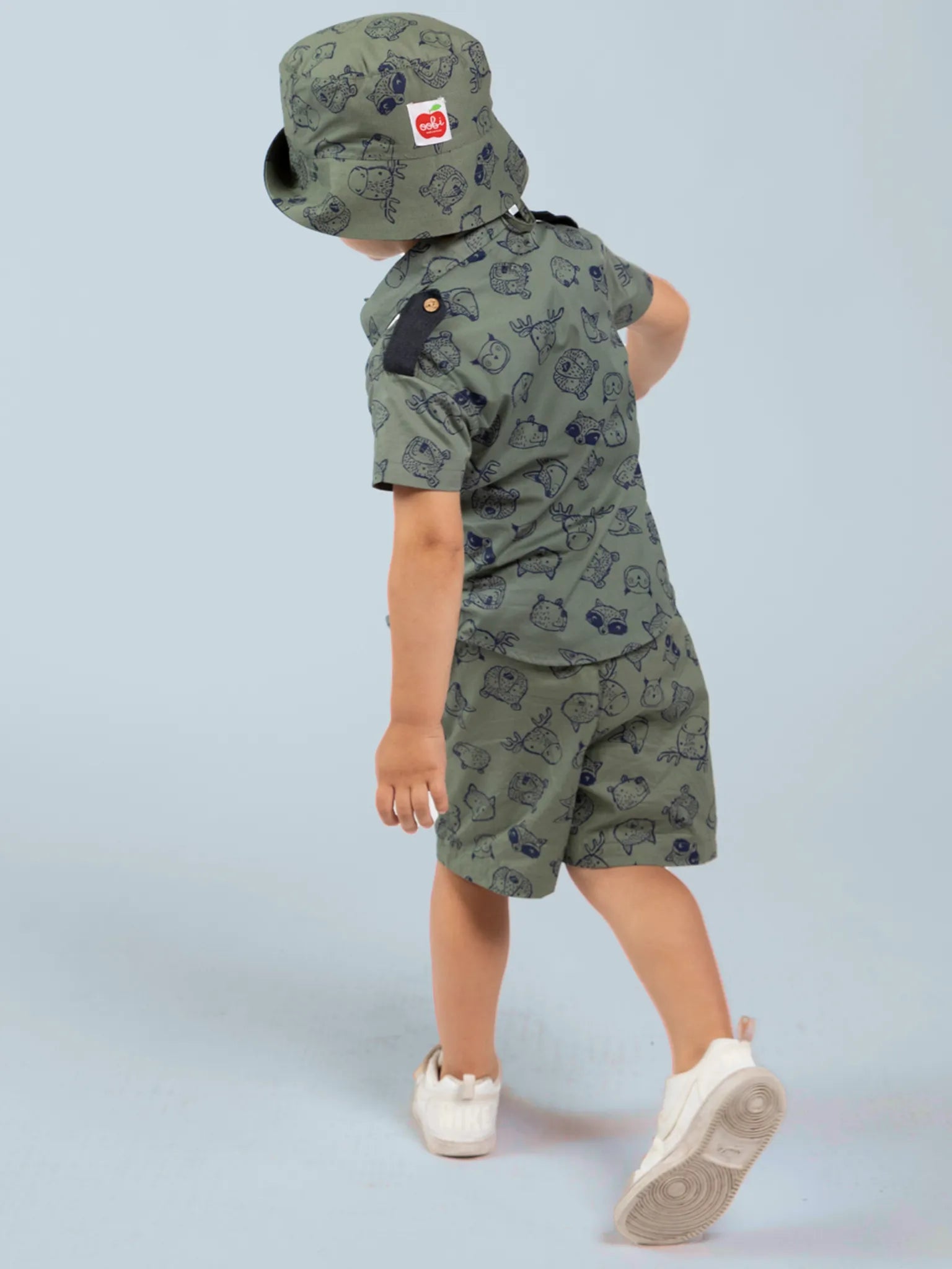 Child wearing an olive green, animal patterned shirt and hat against a light blue background