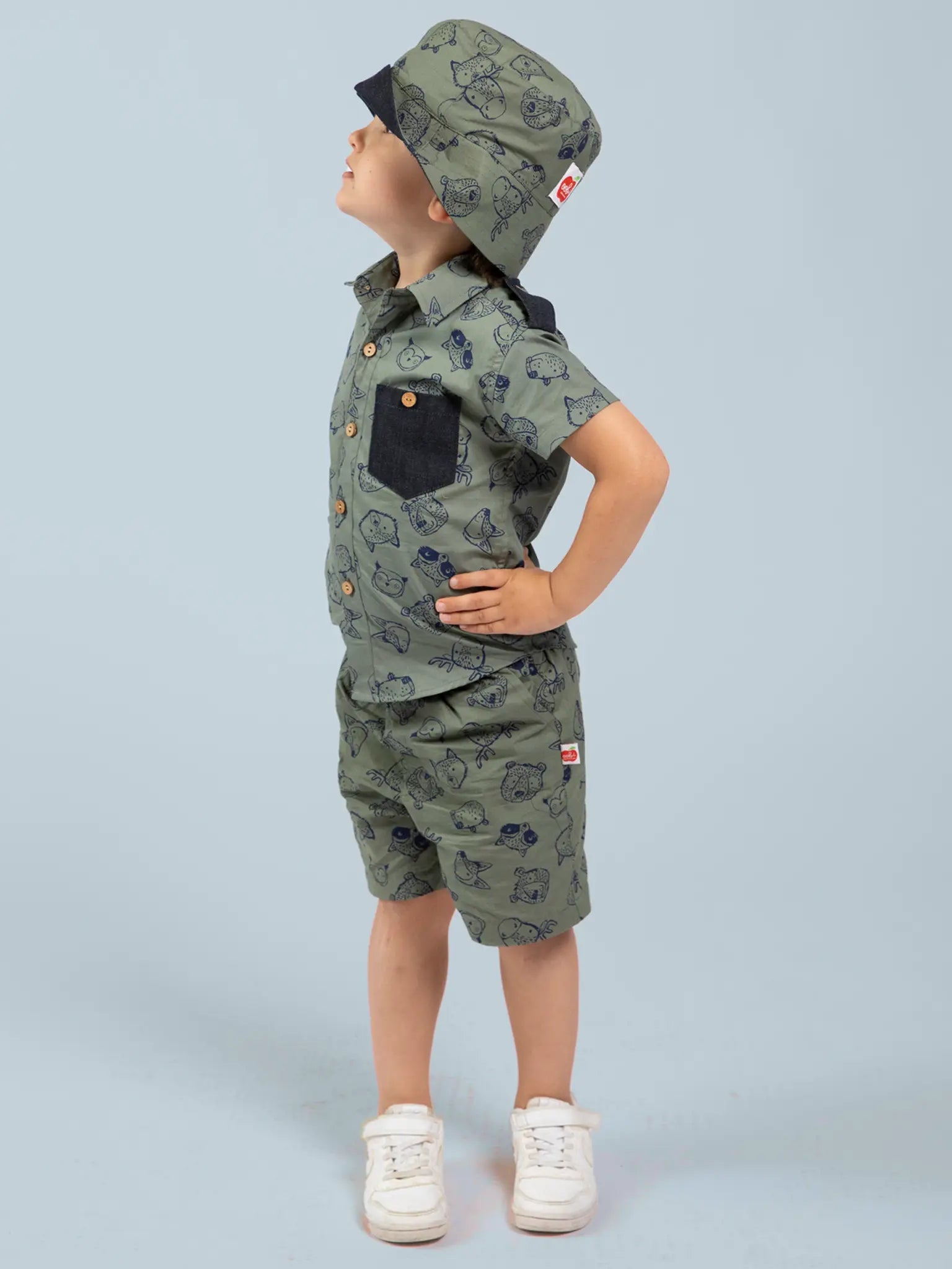 Child wearing an olive green, animal patterned shirt and hat against a light blue background
