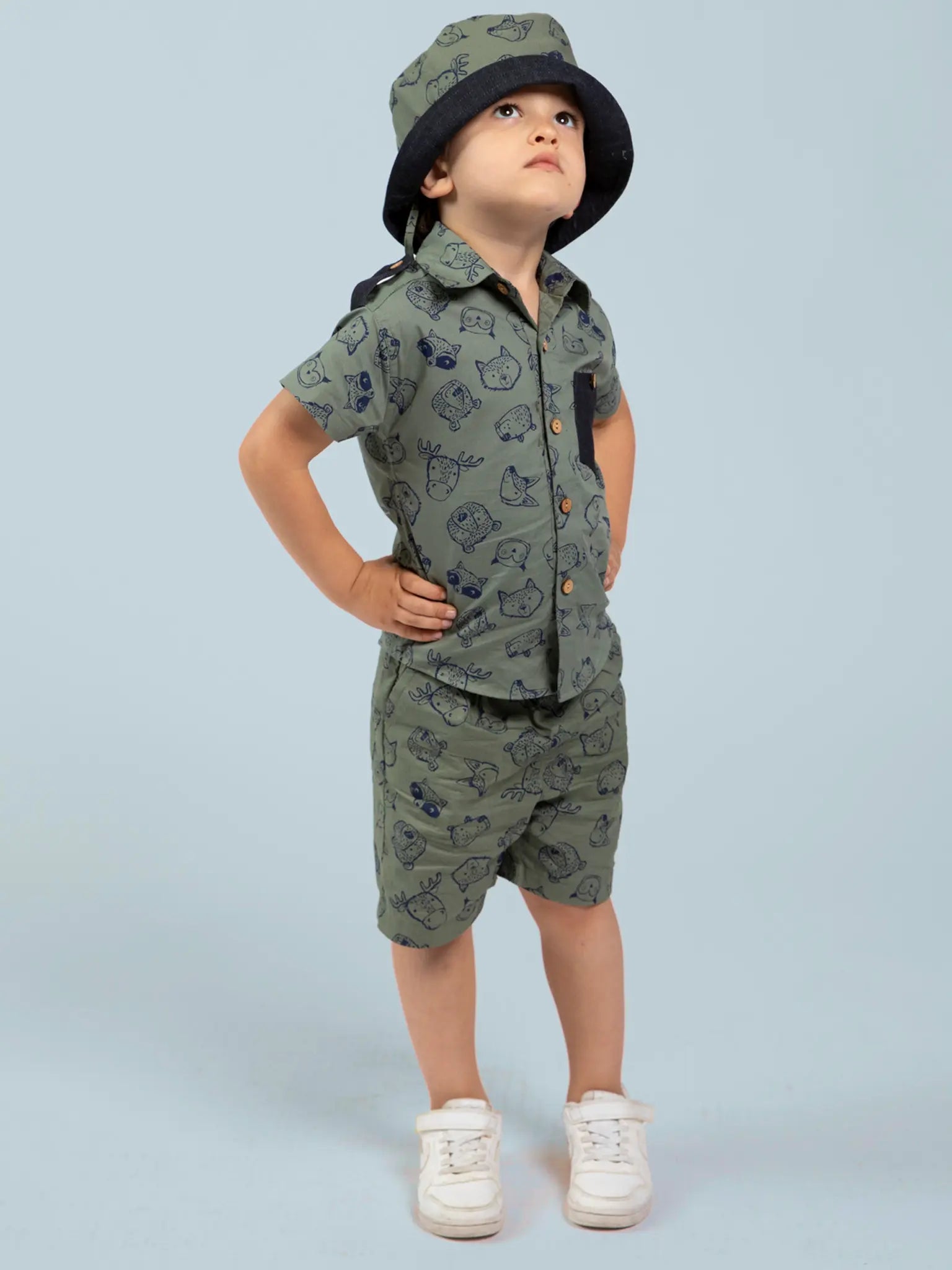 Child wearing an olive green, animal patterned shirt and hat against a light blue background