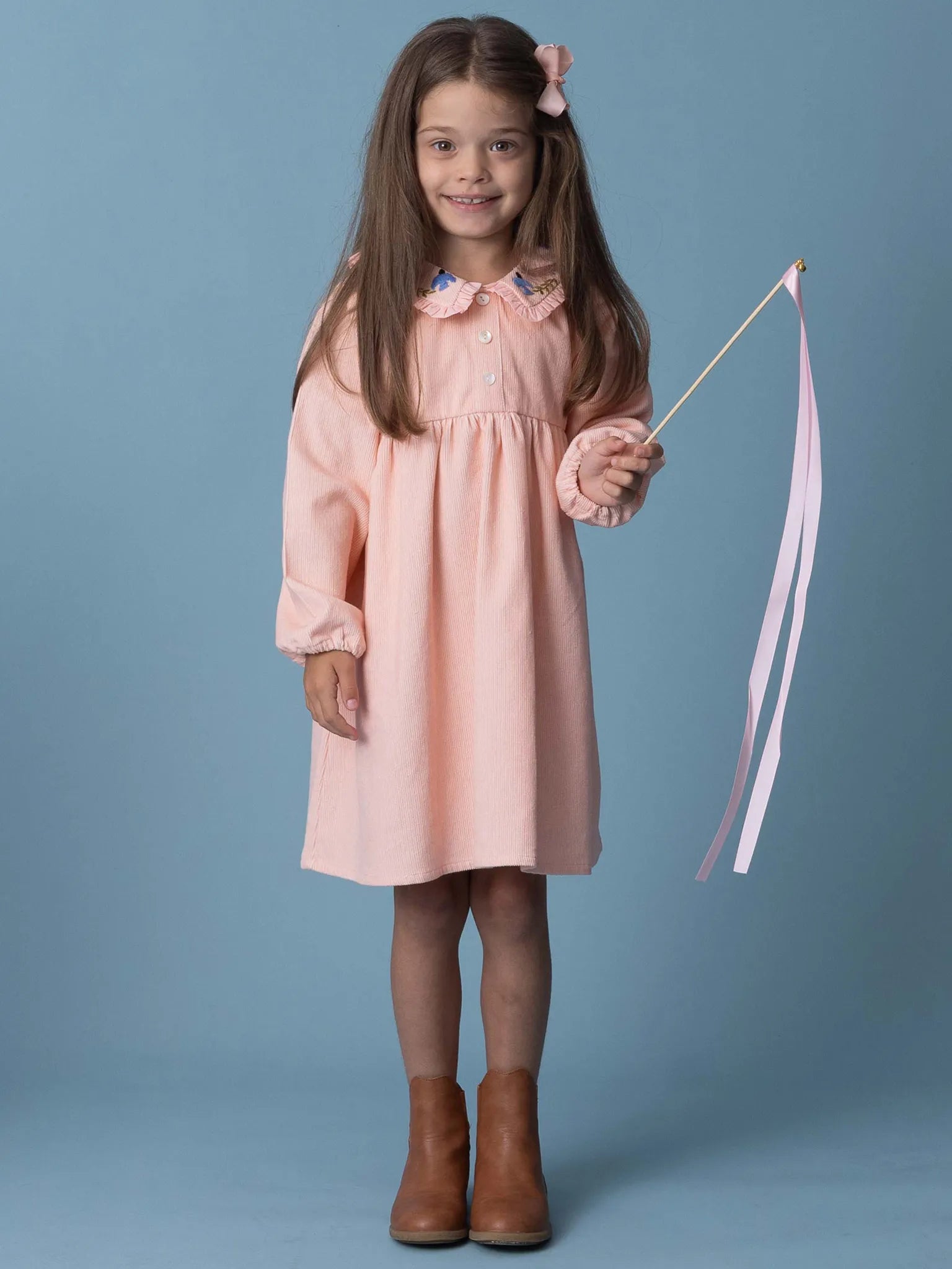 Young girl in a pink dress holding a wand with ribbons against a blue background