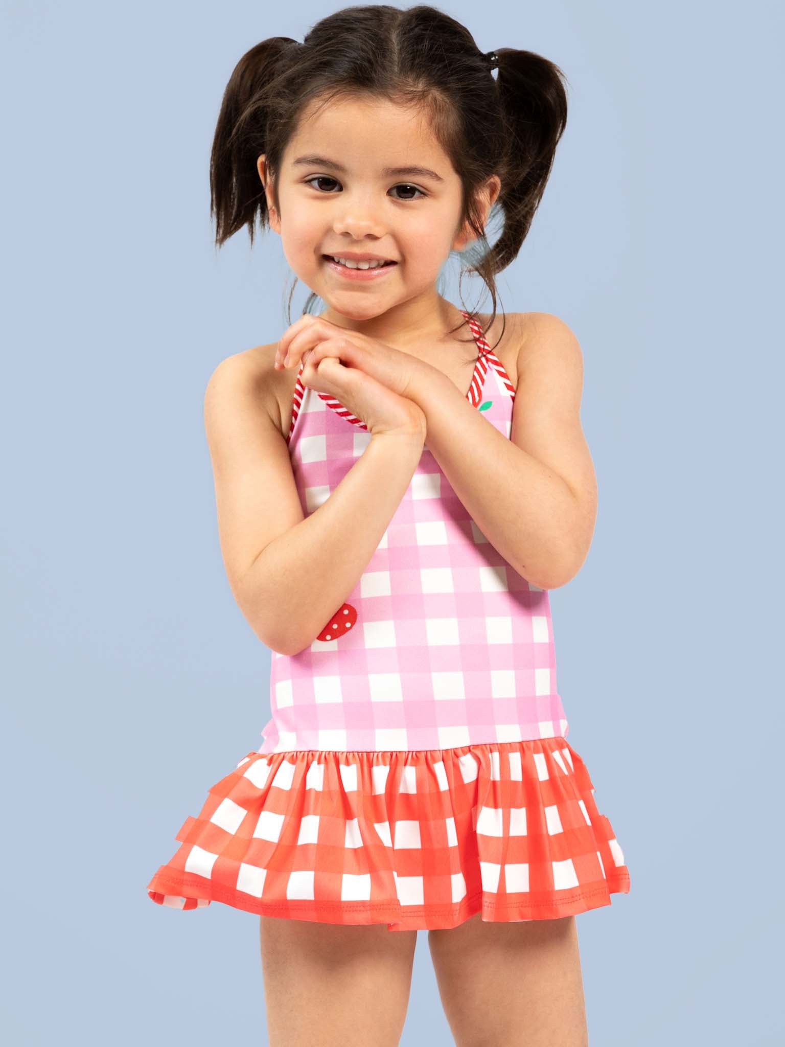 Young girl wearing a pink and red checkered swimsuit against a light blue background