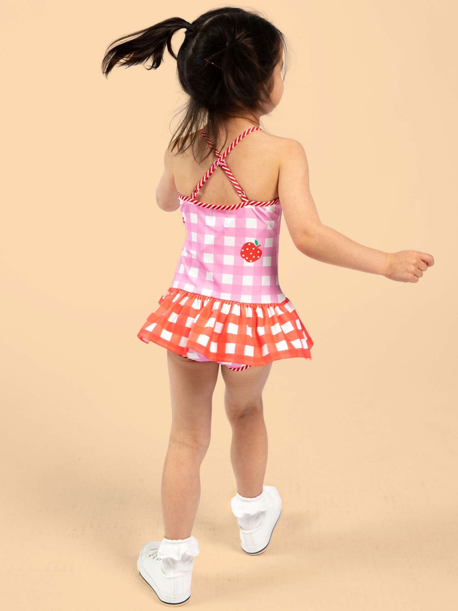 Child wearing a pink and red checkered swimsuit with a flower design on a beige background