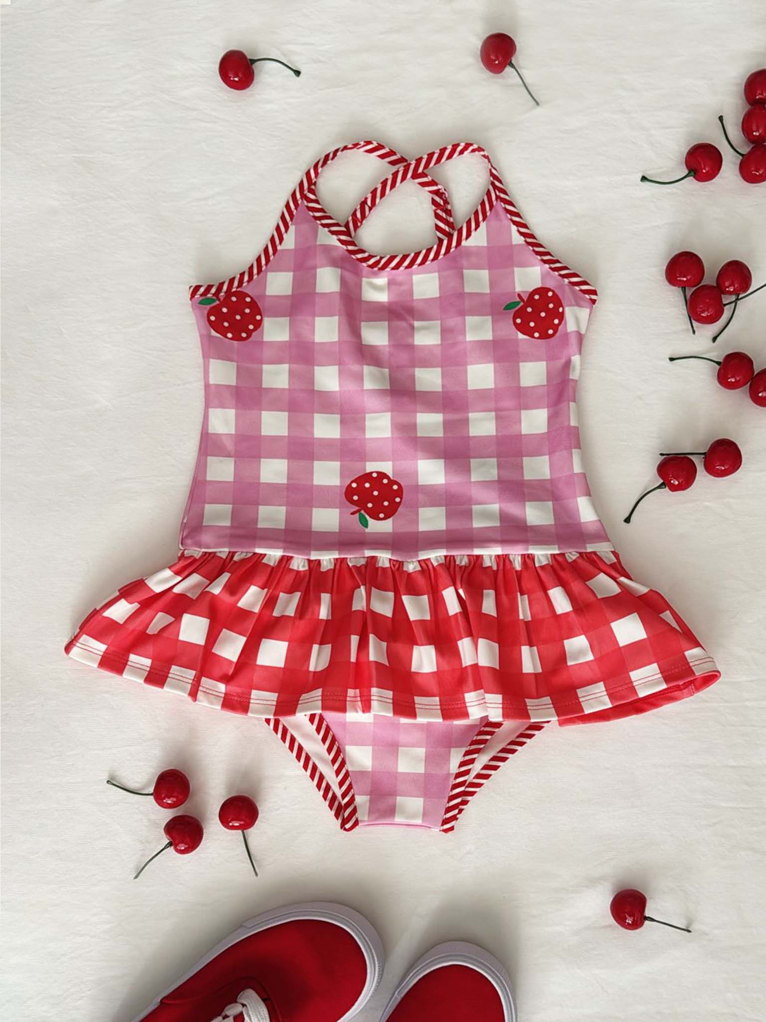 Pink and red checkered children's swimsuit with cherry details on a white background