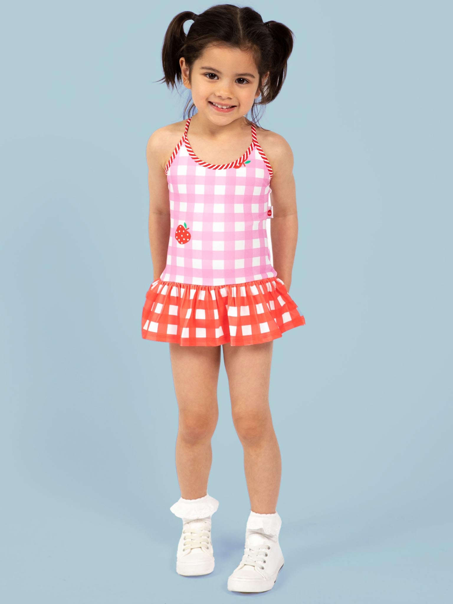 Young girl wearing a pink and red checkered swimsuit with an apple design on a light blue background