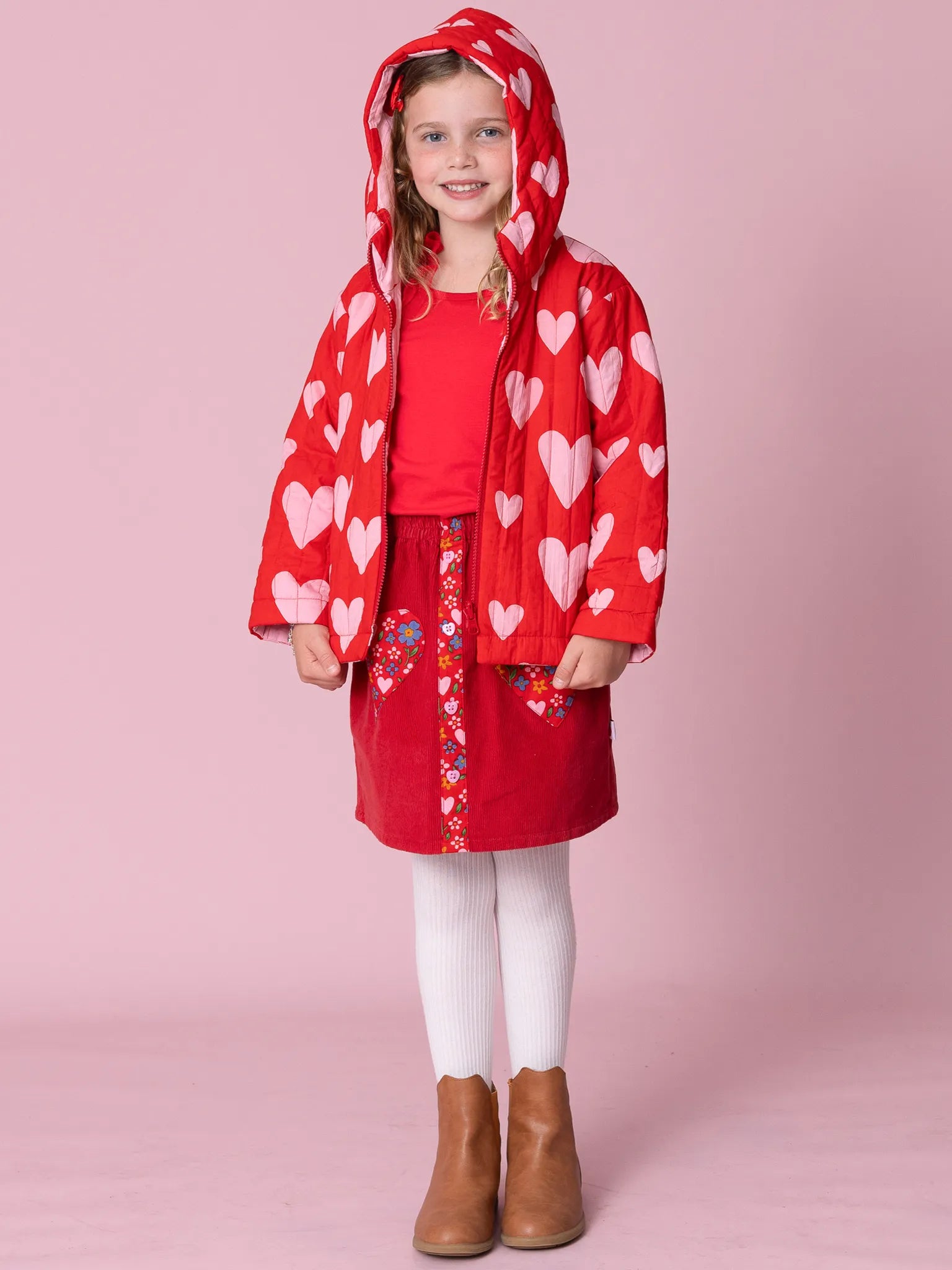 Child wearing a red heart-patterned raincoat on a pink background