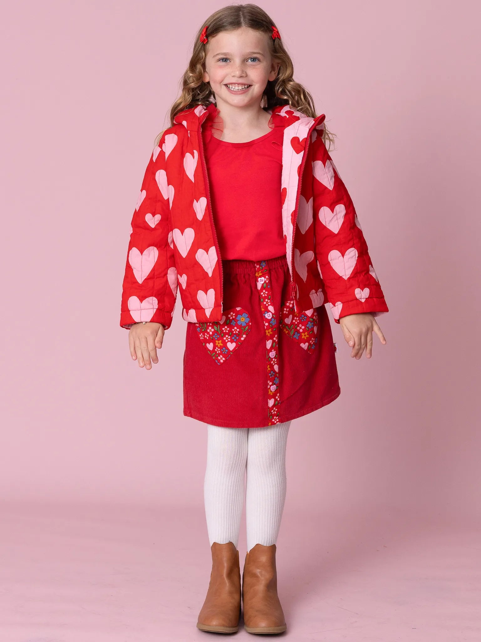 Young girl wearing a red heart-patterned coat against a pink background