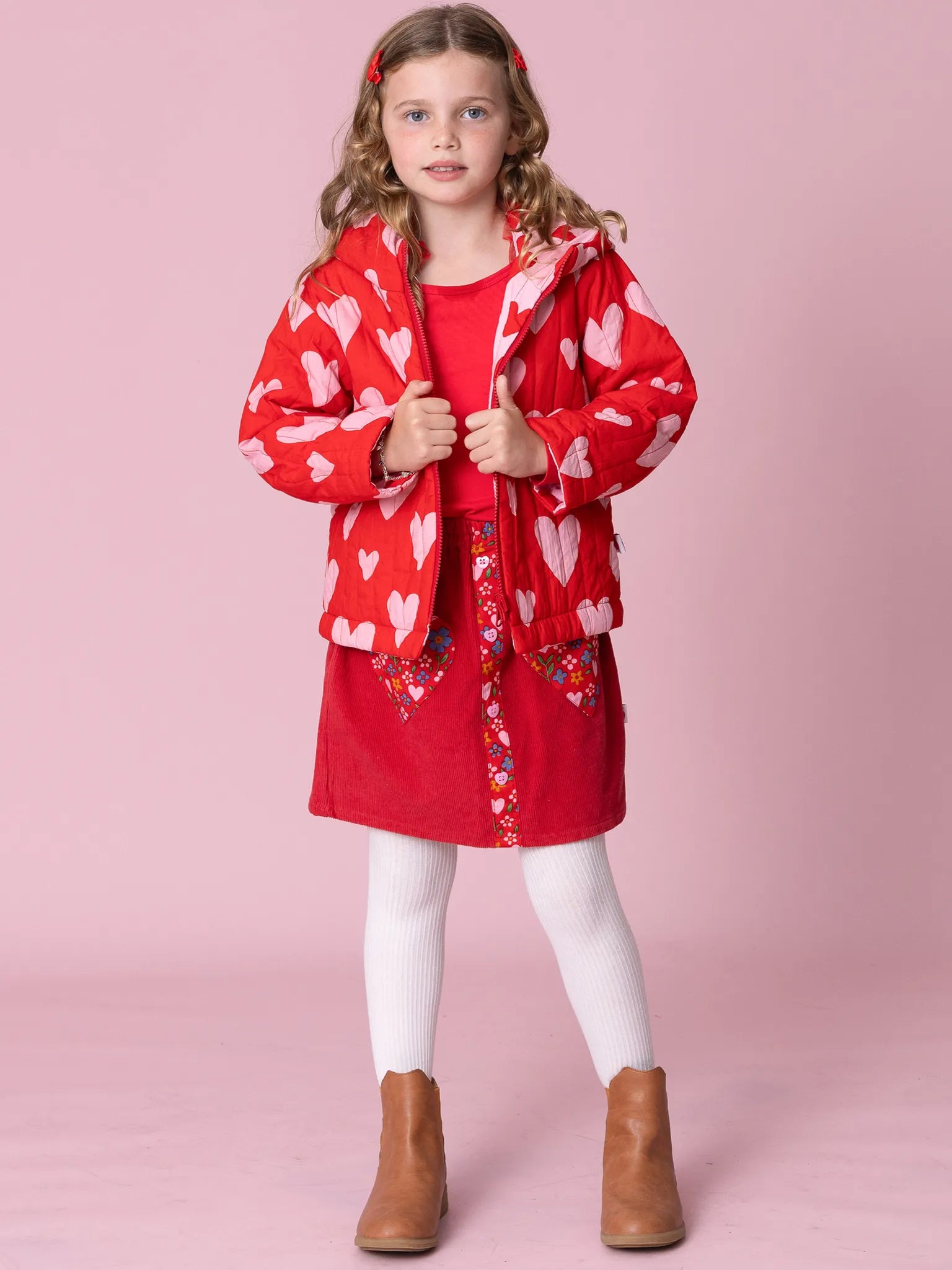 Young girl wearing a red heart-patterned coat on a pink background