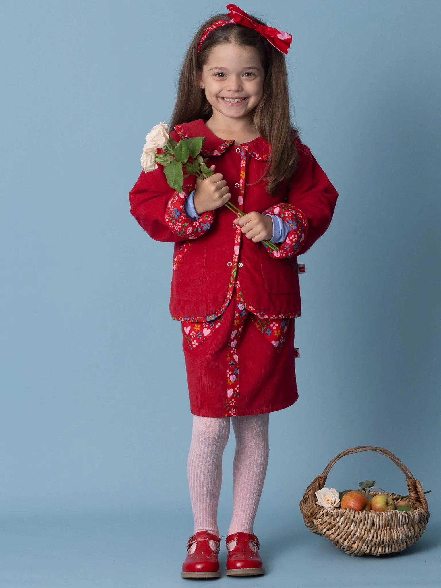Young girl in a red outfit with a basket of apples on a blue background