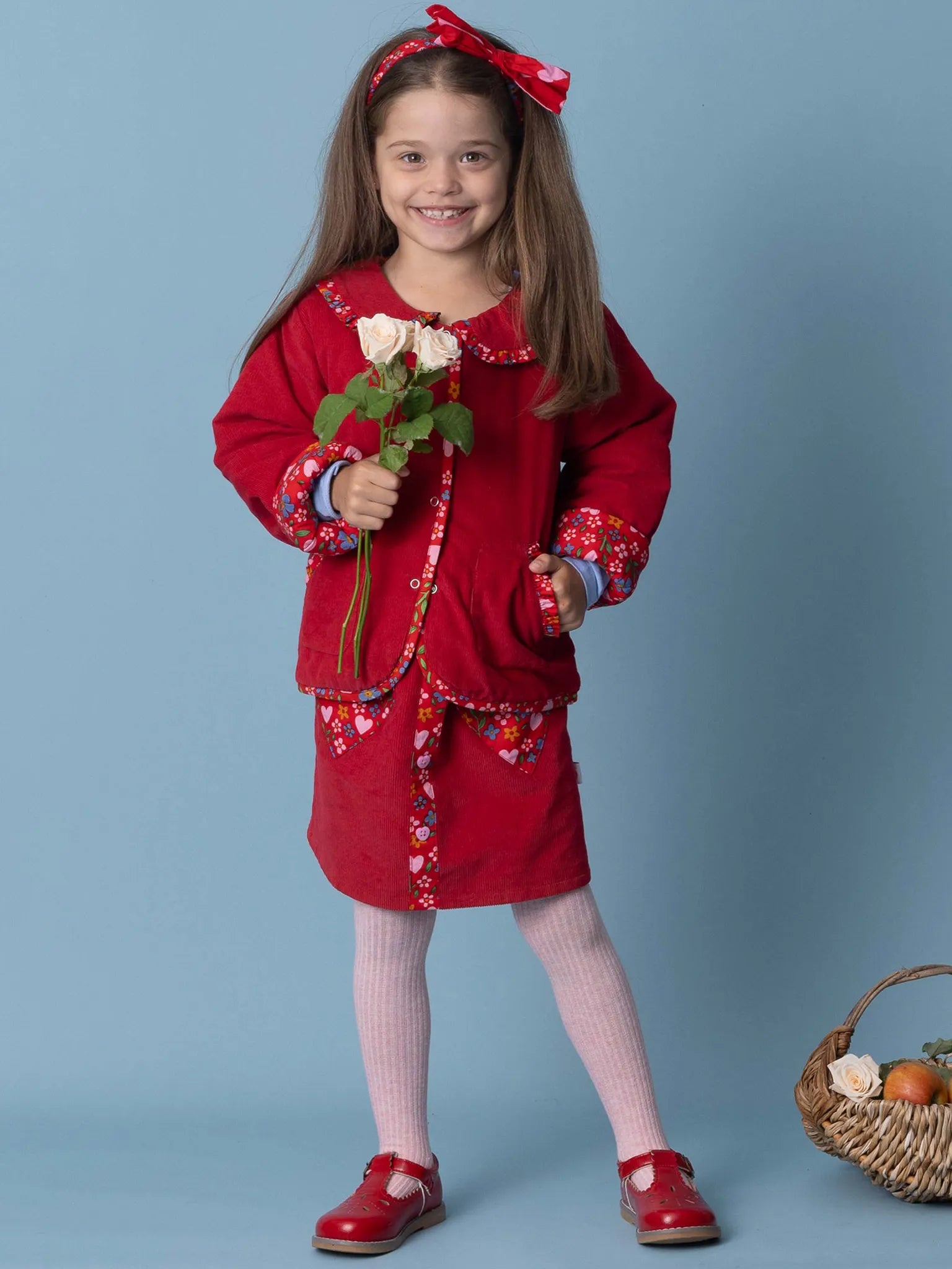 Young girl in a red outfit holding flowers against a blue background