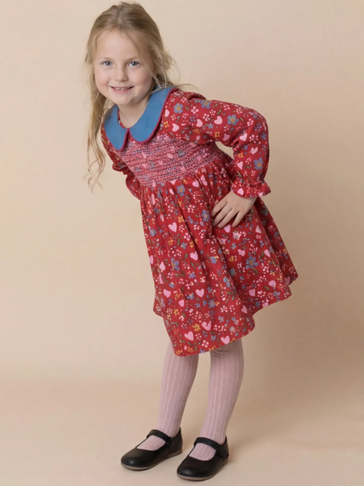 Young girl wearing a red patterned dress with a blue collar against a beige background