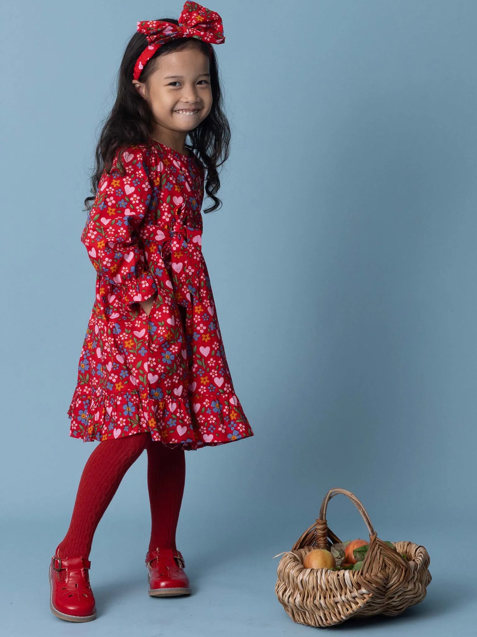 Young girl in a red floral dress with a basket of pumpkins on a blue background