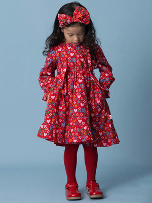 Young girl wearing a red floral dress with matching headband and shoes on a blue background