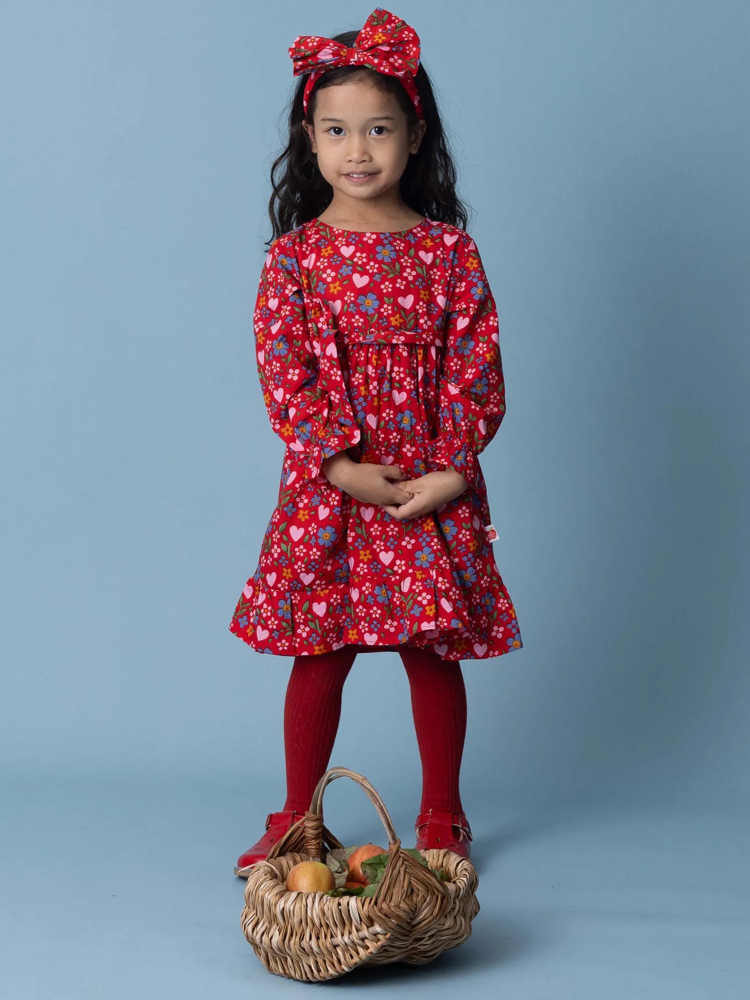 Young girl in a red floral dress with a basket of fruits on a blue background