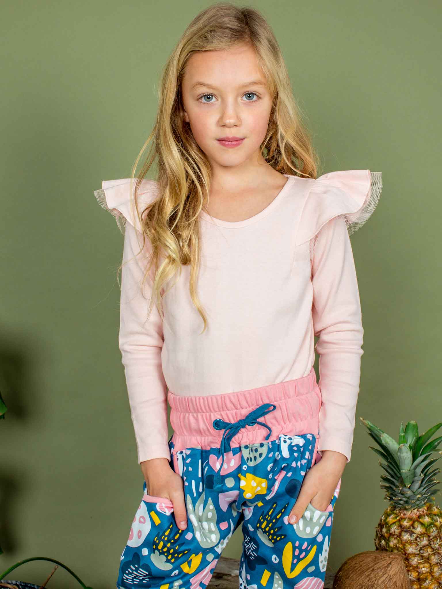 Young girl wearing a pink top and colorful pants against a green background