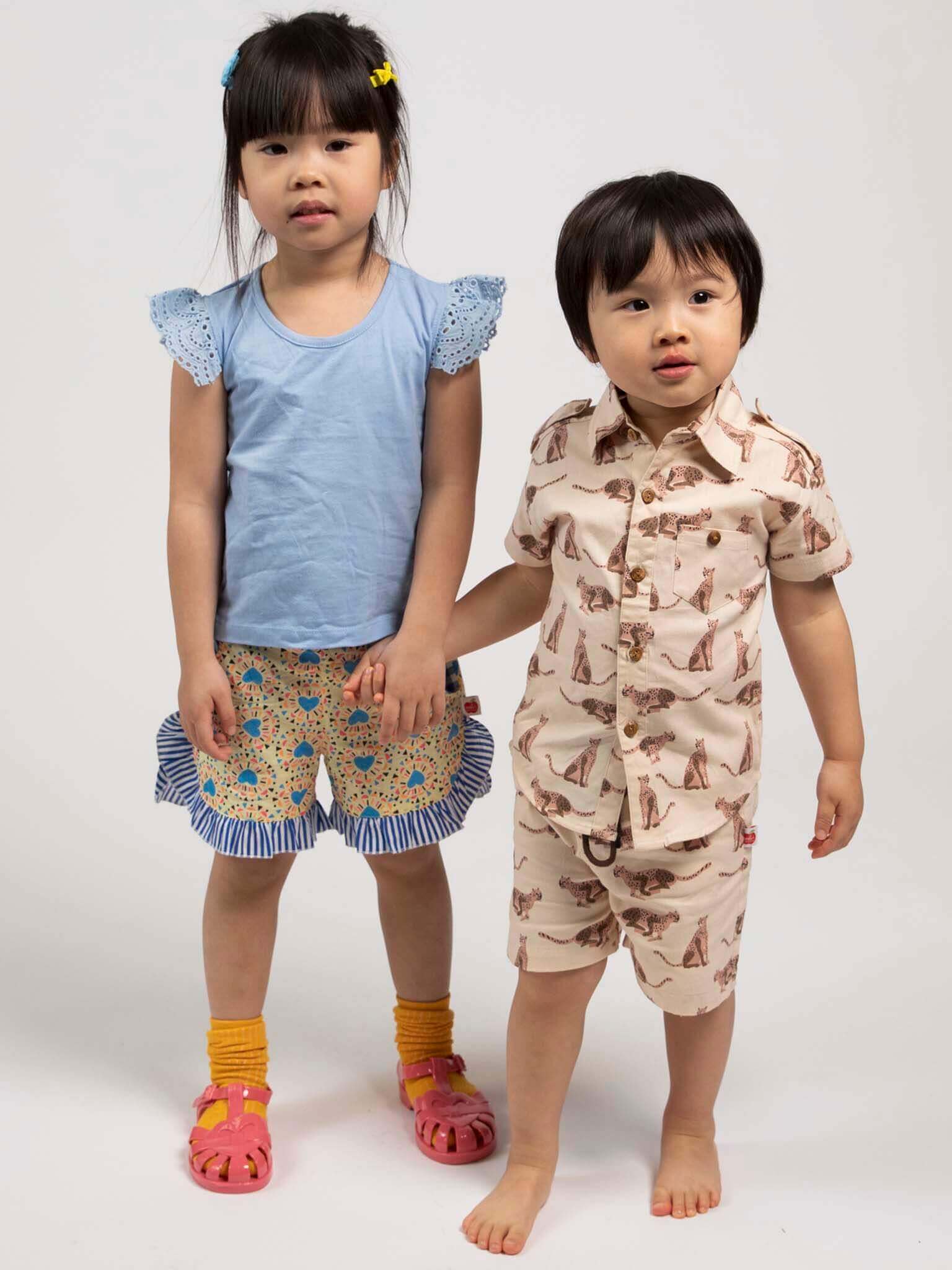 Two children holding hands, wearing colorful outfits on a white background