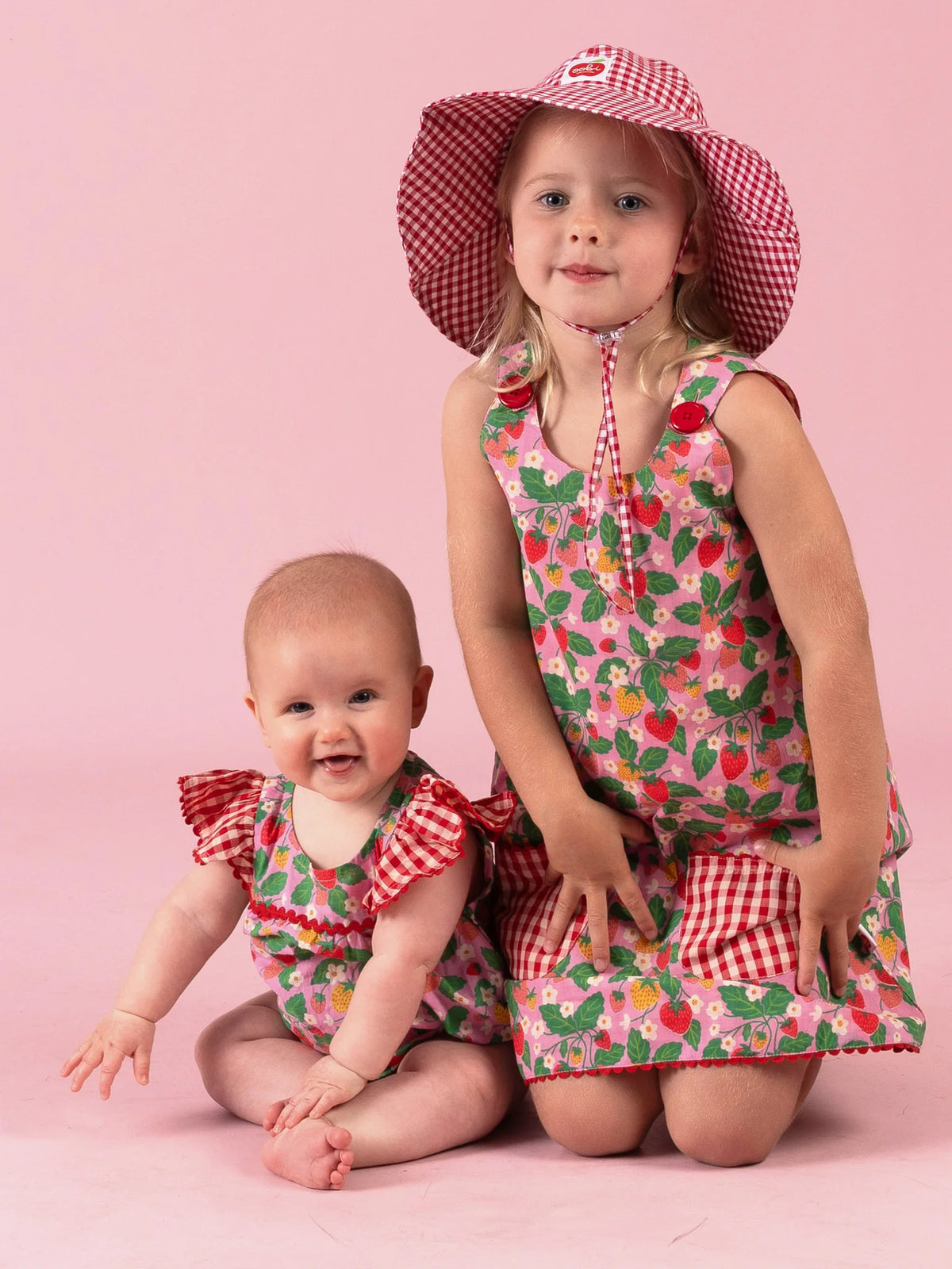 Girl in the Strawberry Fields Gracie dress kneeling beside a baby in the Strawberry Fields romper